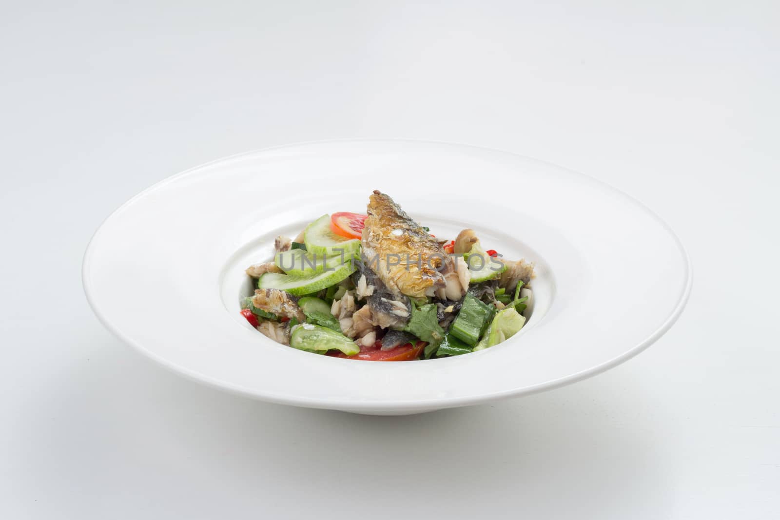 Thai appetizer - spicy mackerel salad with lemon grass, shallots, raw mango, chili and lettuce on a white plate