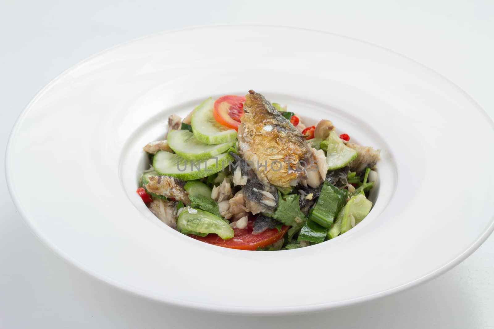 Thai appetizer - spicy mackerel salad with lemon grass, shallots, raw mango, chili and lettuce on a white plate