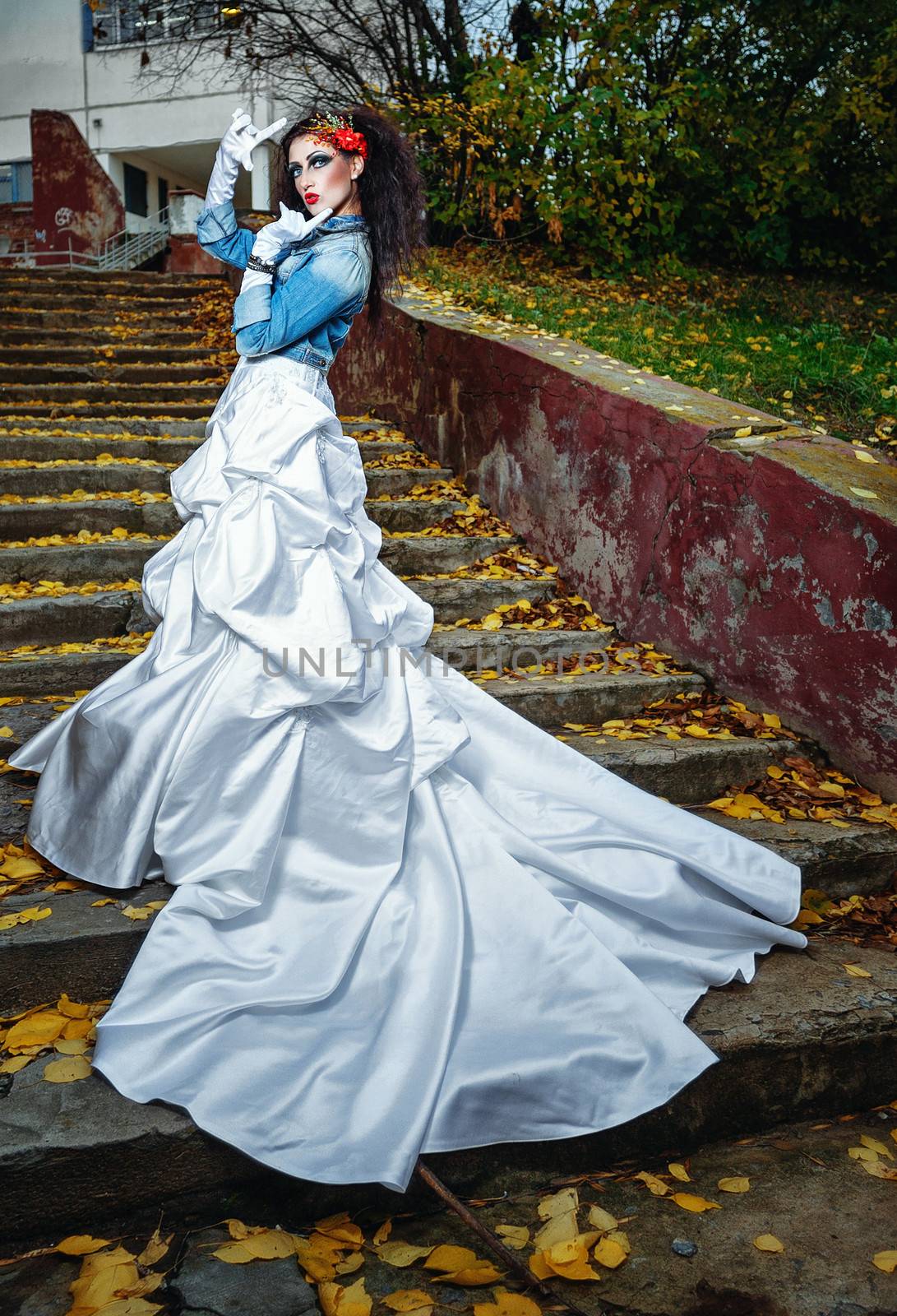 Beautiful bride in magnificent dress stands alone on stairs in autumn day