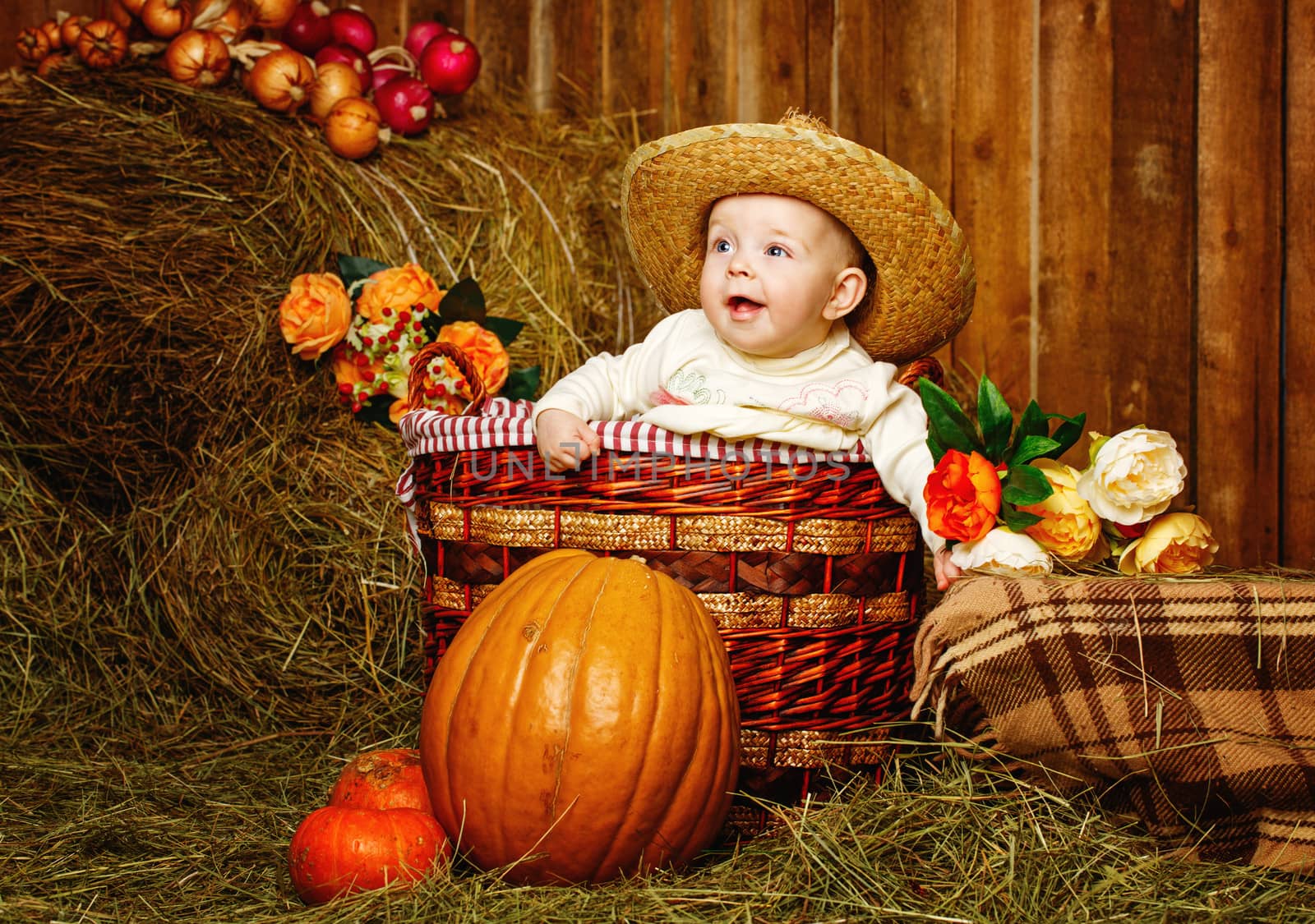 Little girl in straw hat sitting in a wicker basket near pumpkins