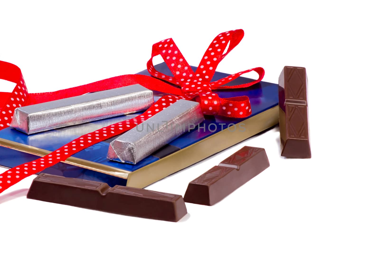 Blue box with chocolate slices wrapped in foil and decorated with a red ribbon. Presents on a white background.
