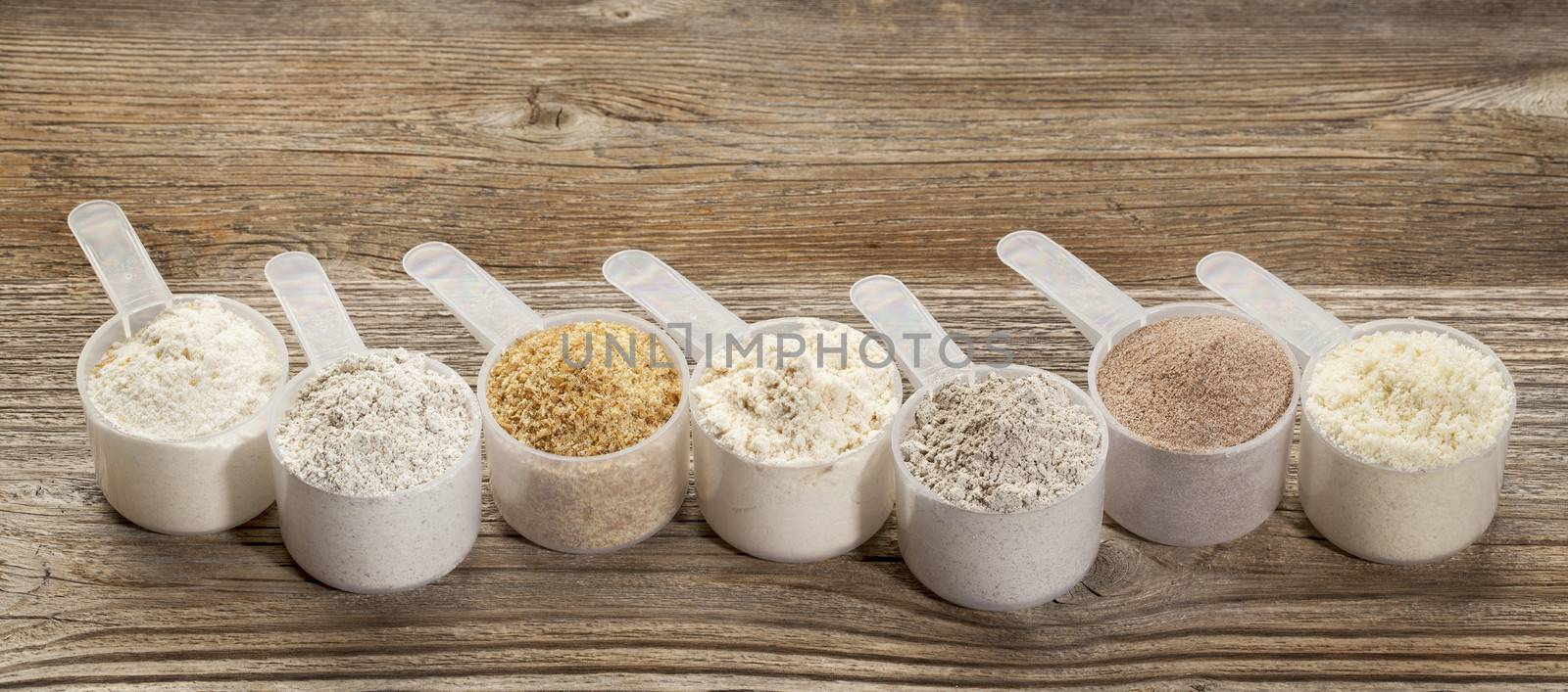 a row of measuring scoops of gluten free flours - almond, coconut, teff, flaxseed meal, whole rice, brown rice, buckwheat