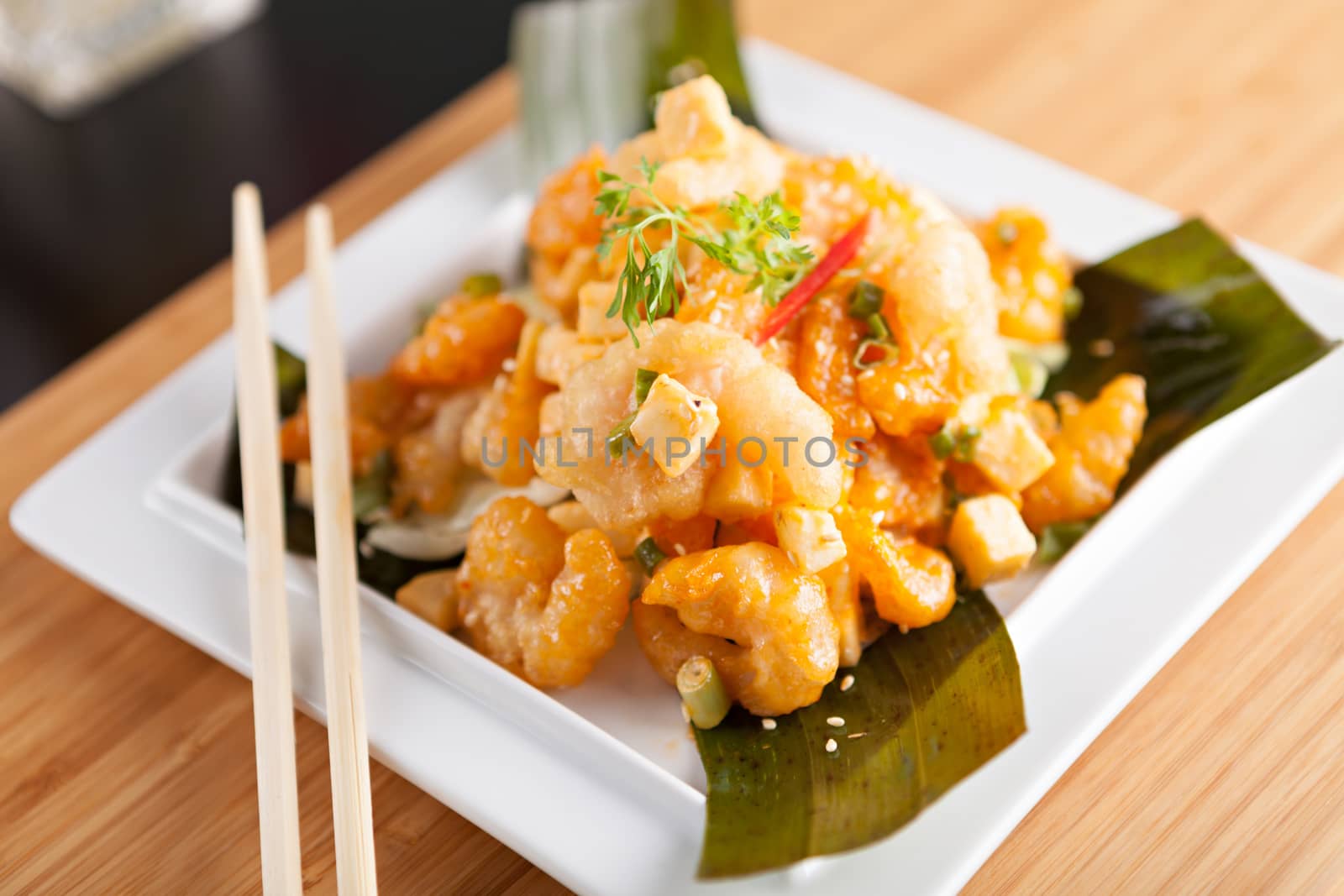 Thai crispy shrimp dish with apple and sesame seeds presented beautifully on a white square plate with chopsticks.