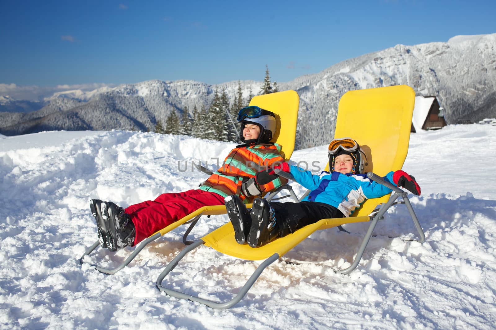 Winter, ski, sun and fun - kids in winter resort resting in the deck chair