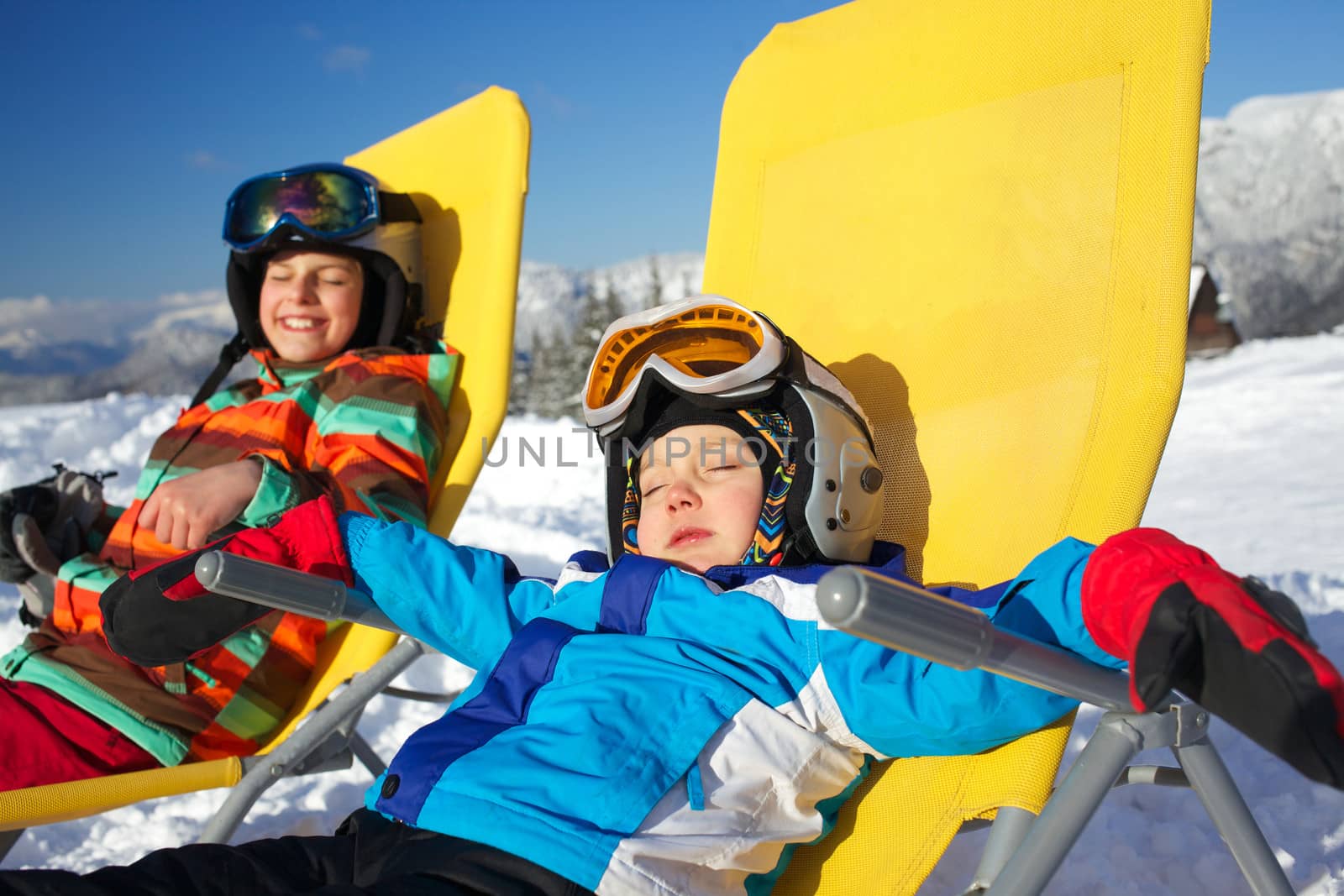Winter, ski, sun and fun - portrait of kids in winter resort resting in the deck chair