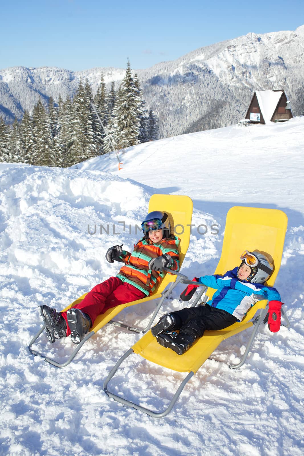 Winter, ski, sun and fun - kids in winter resort resting in the deck chair