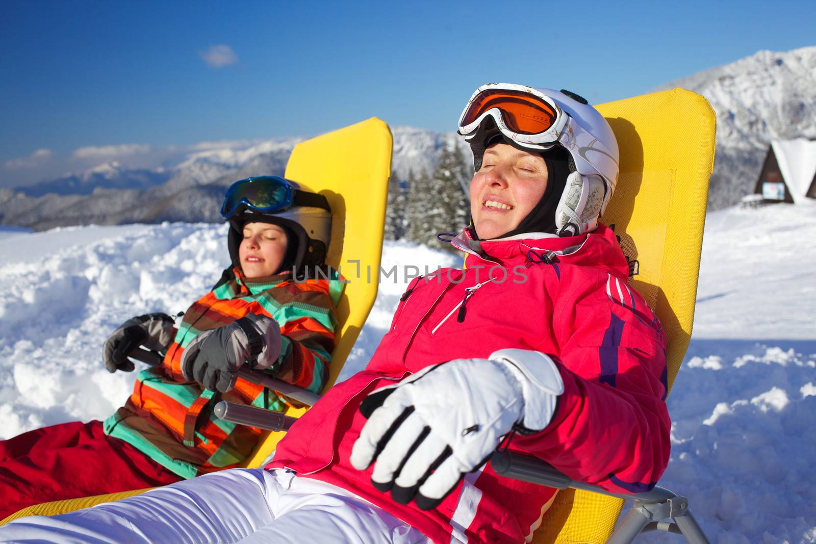 Winter, ski, sun and fun - Portrait of mother with her daughter in winter resort resting in the deck chair