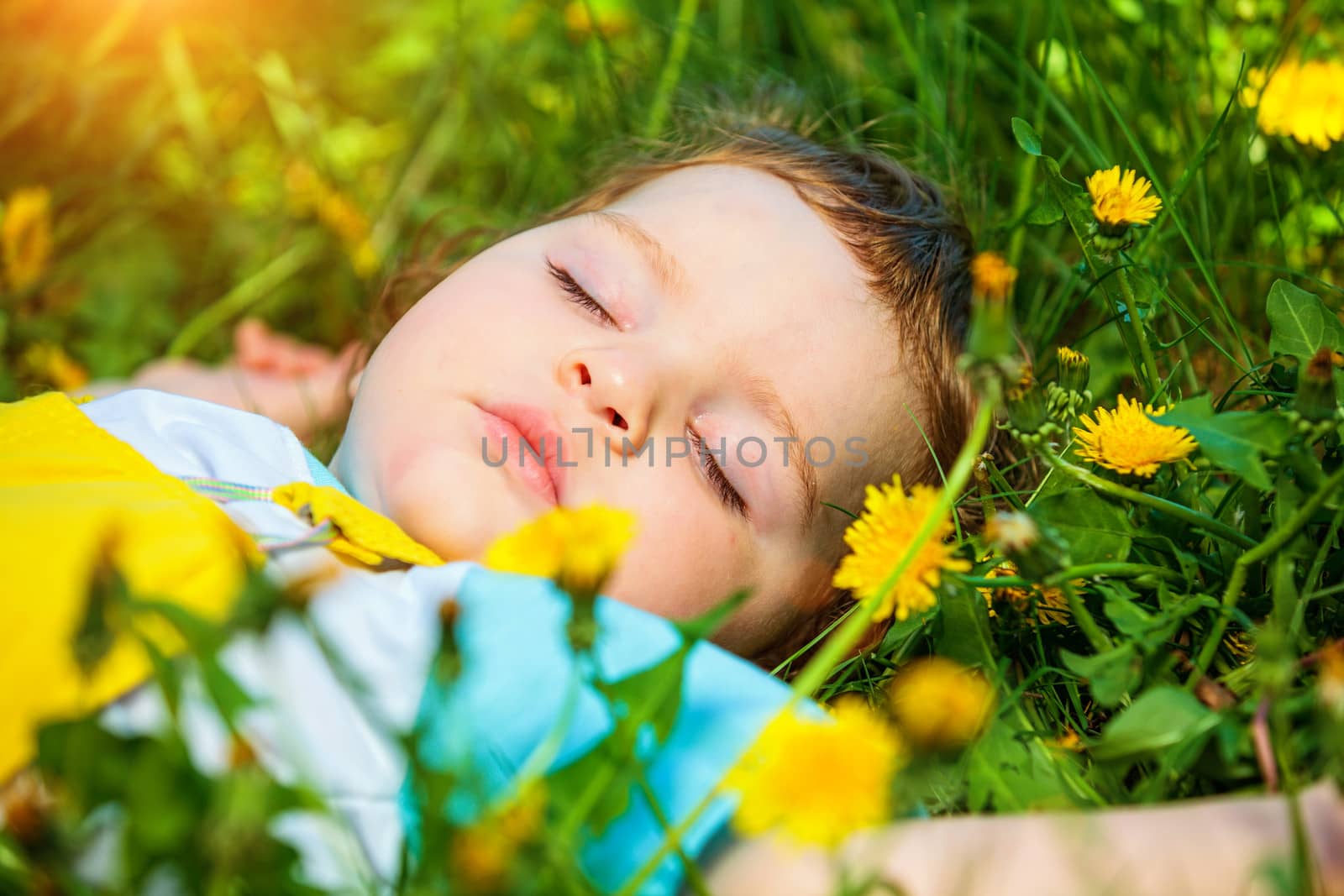 Closeup portrait of a little baby boy sleeping outdoors on grass.