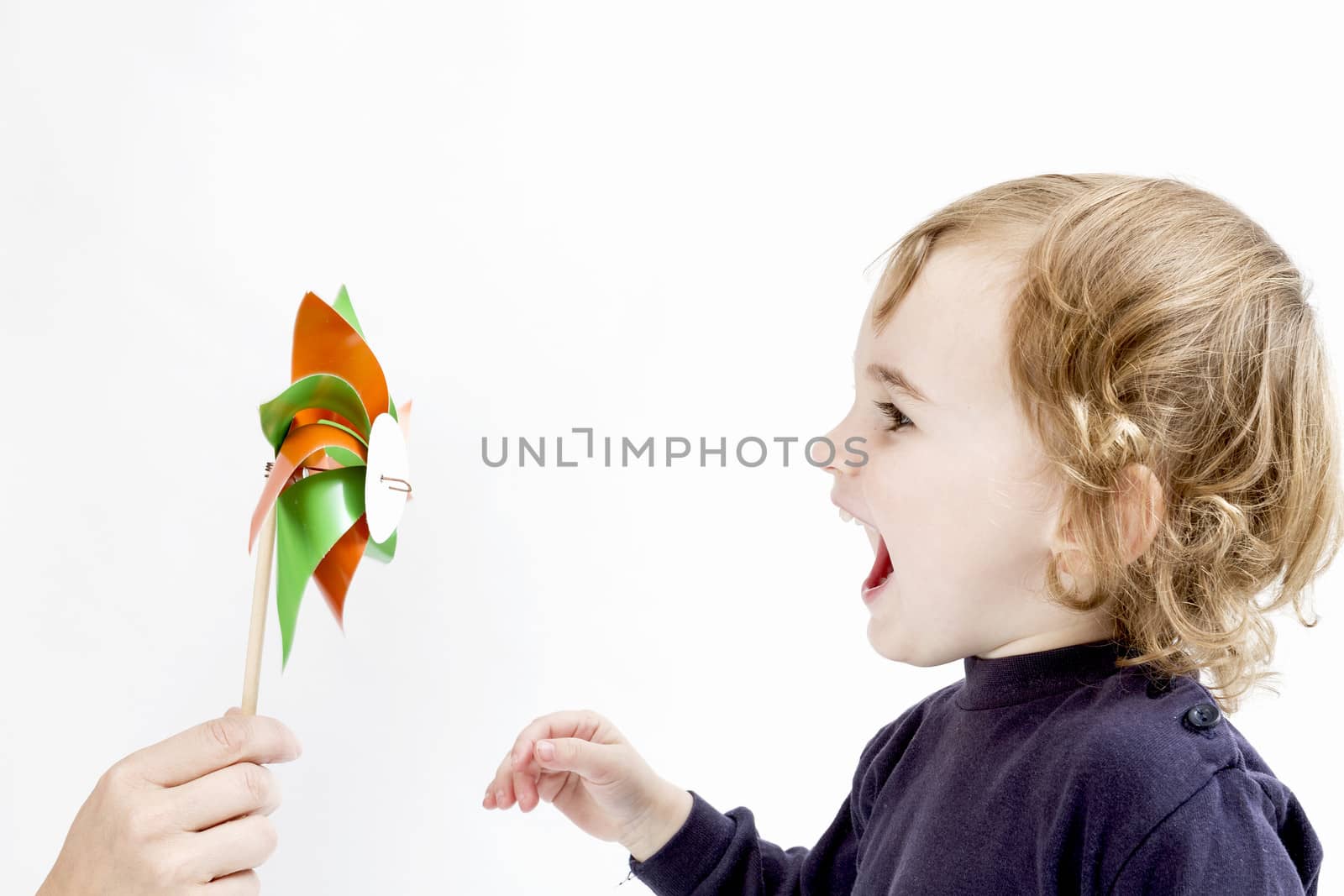 cute girl blowing to colorful windmill. studio shot in light grey background