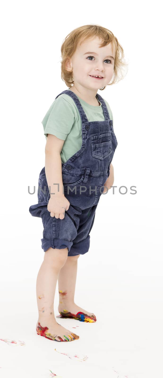 child with painted feet holding trousers up. studio shot in grey background