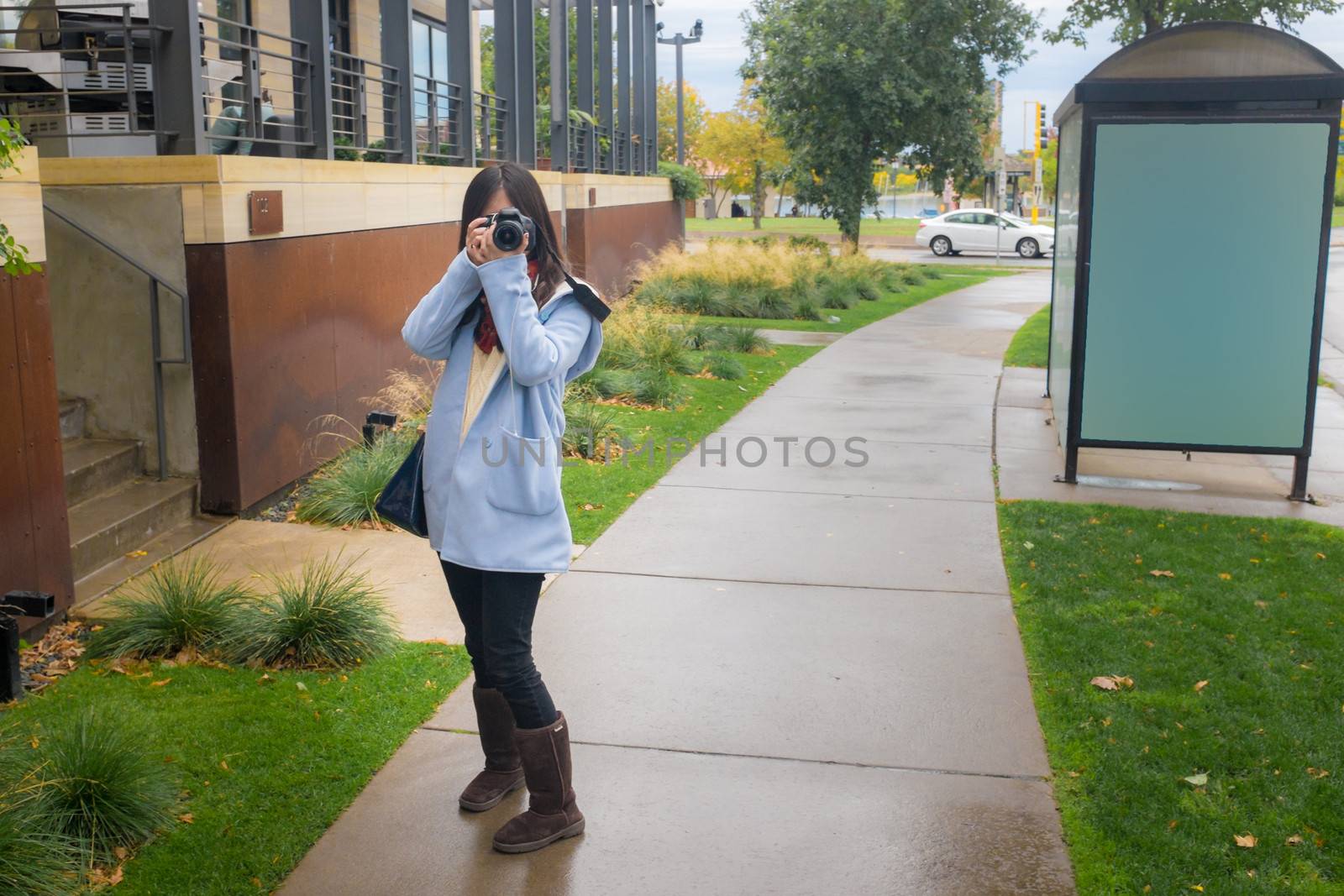 Girl photographer with camera on a public side walk during autumn listening to music