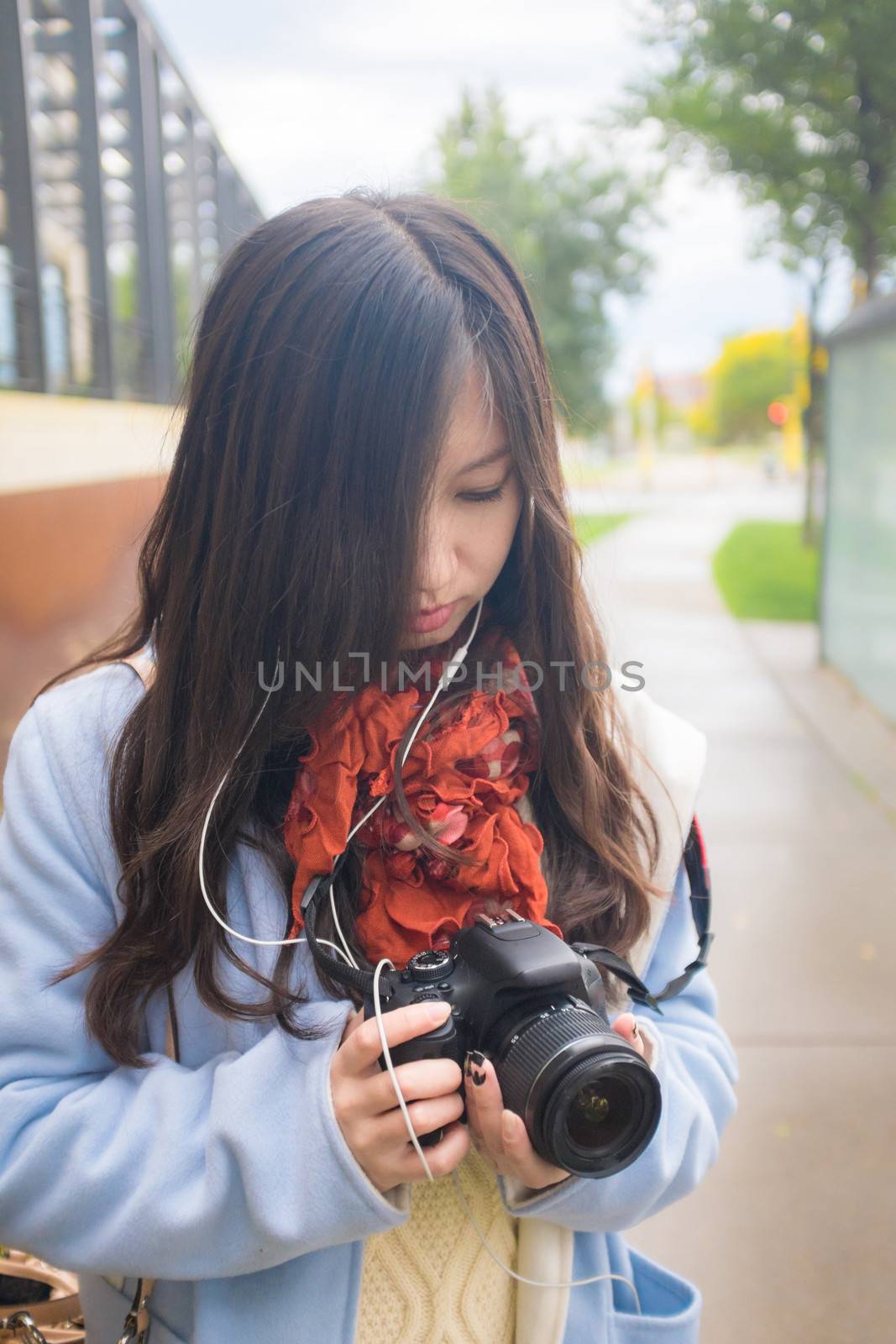 Girl photographer with camera on a public side walk during autumn listening to music