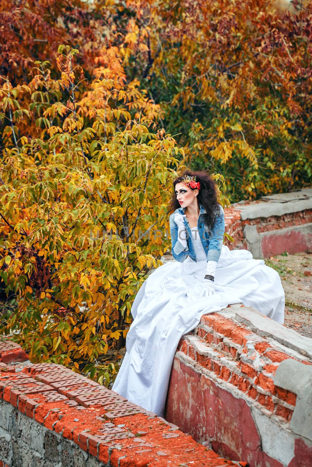 Beautiful bride in wedding dress and denim jacket in autumn park