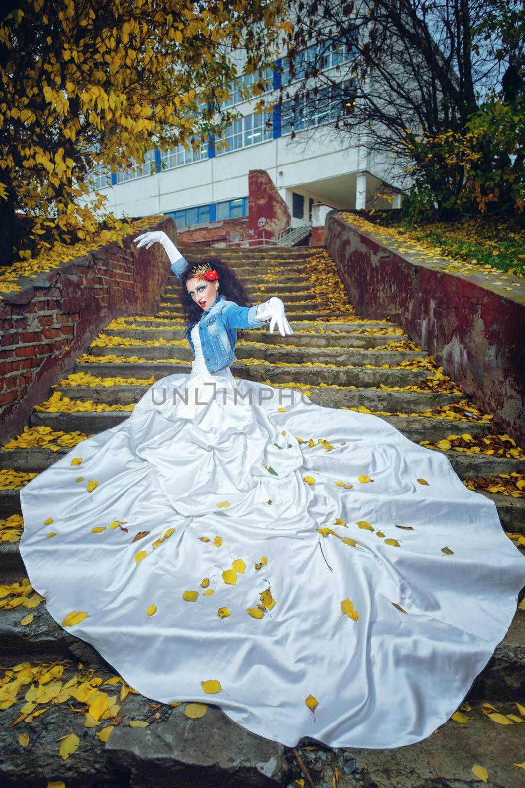 Beautiful bride in magnificent dress stands alone on stairs in autumn day