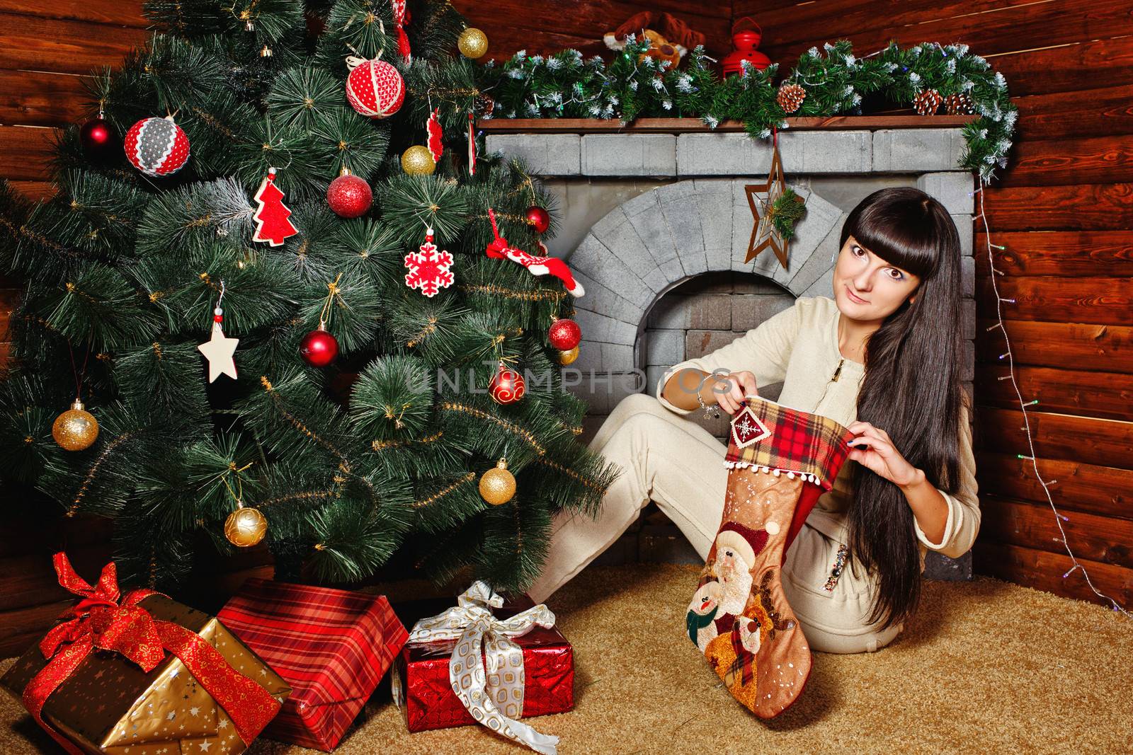 Attractive young woman holding gift and sits near Christmas tree