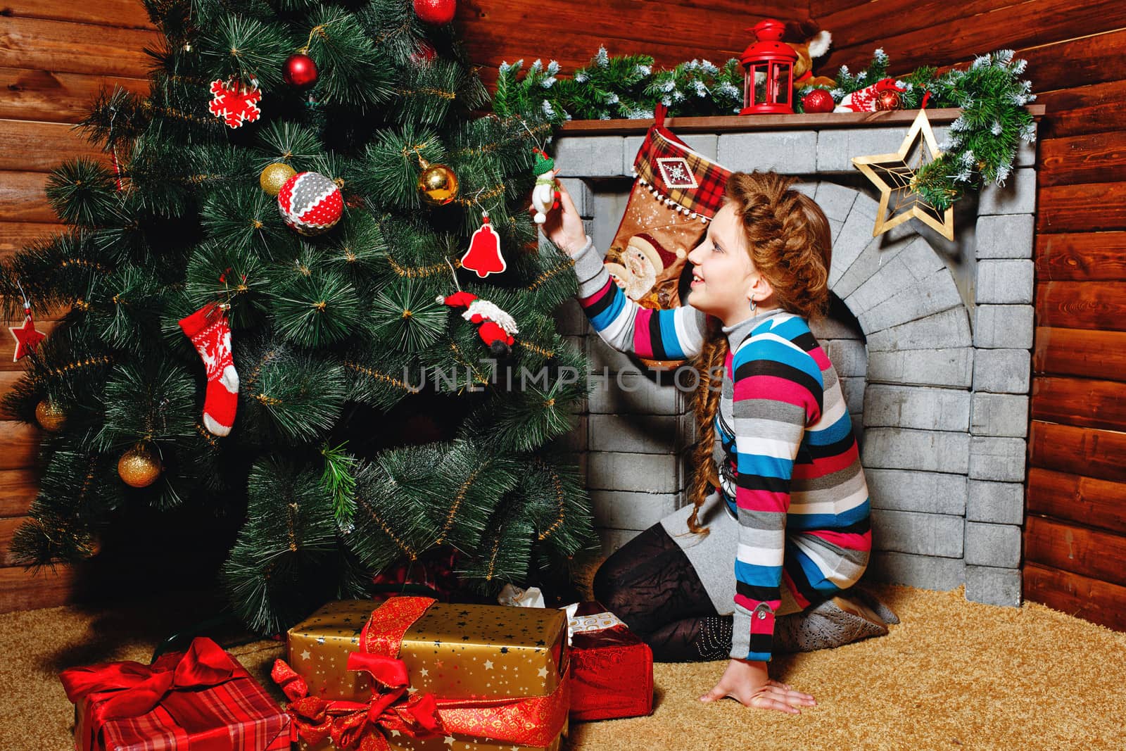Cute little girl decorates Christmas tree under which gifts are