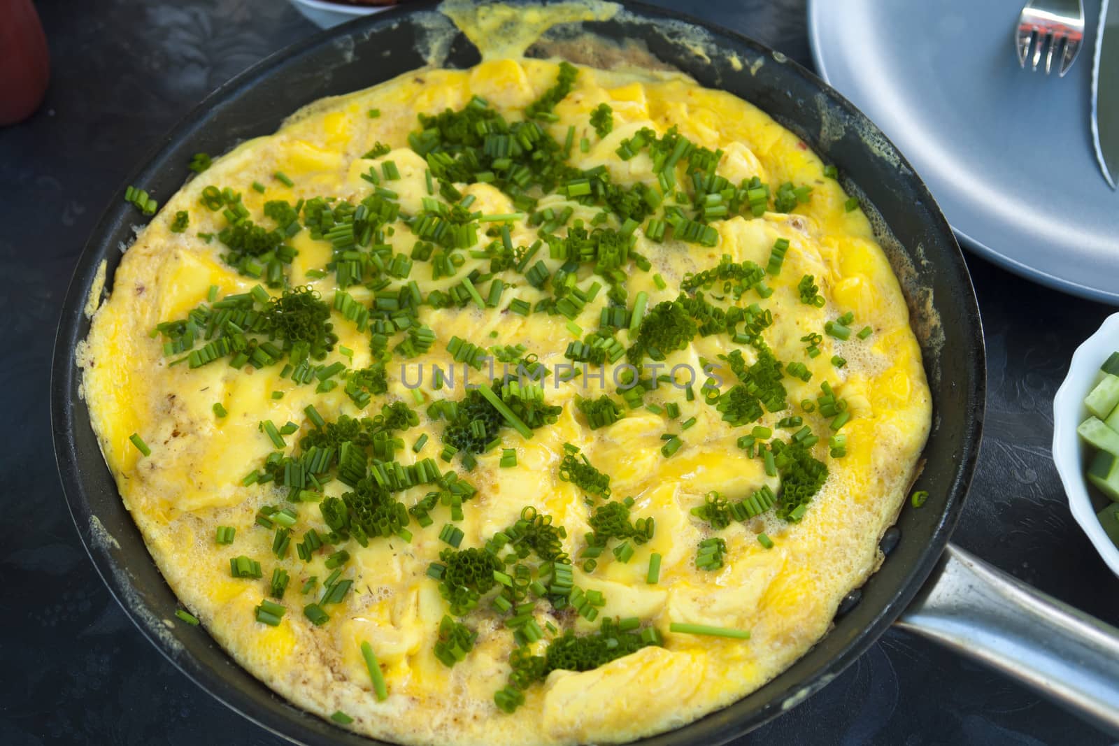 Omelet scrambled eggs with chives and herbs in a frying pan