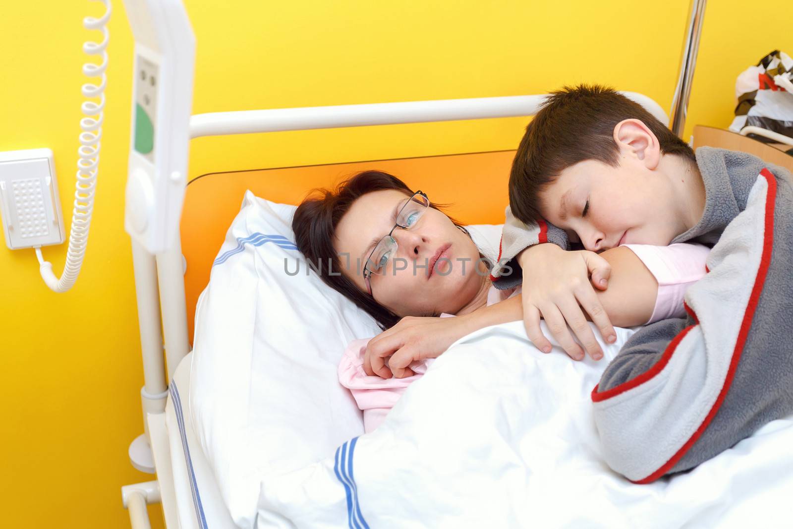 sad middle-aged woman lying in hospital with son by artush