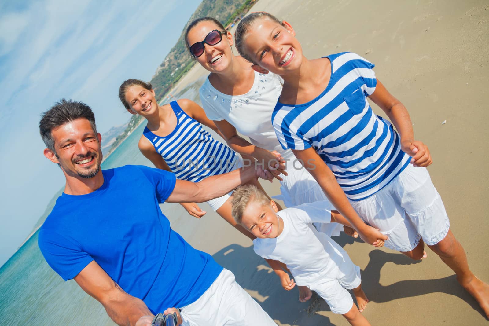 Photo of happy family with three kids running down the beach