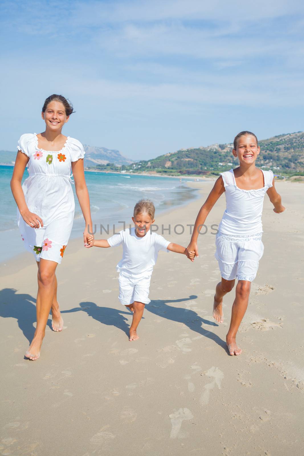 Adorable happy boy and girls running on beach vacation. Vertical view