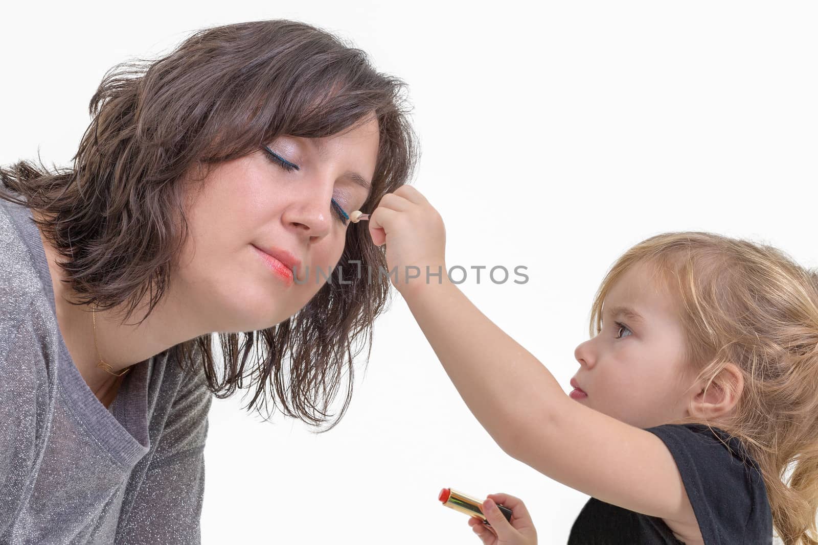 Adorable litte blond girl applying makeup to her mother putting eyeshadow on her eyes, isolated on white