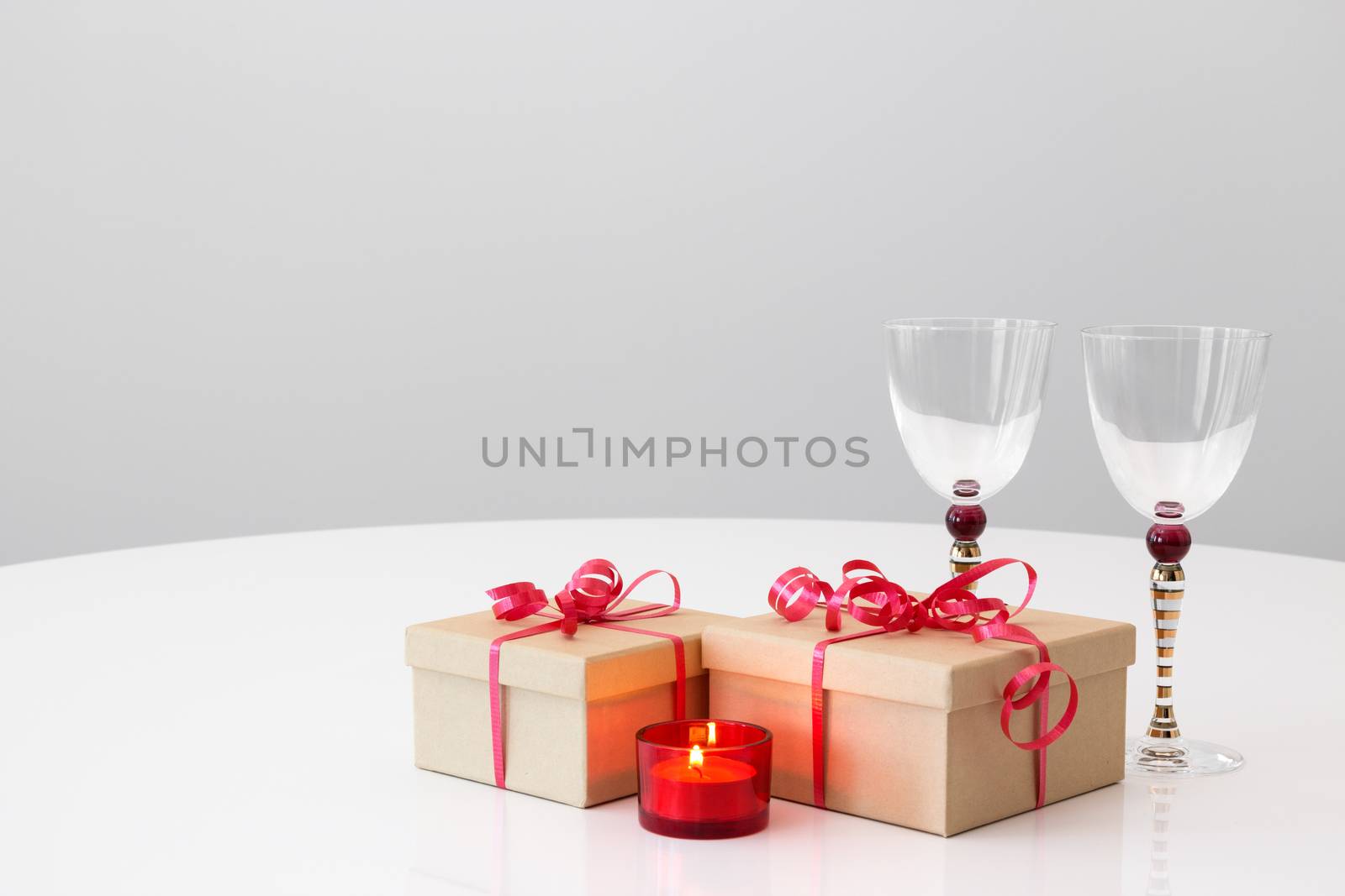 Gifts with red ribbons, wineglasses and candlelight on a table.