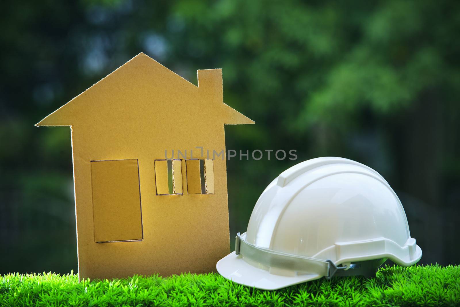 paper home out line with safety helmet on green grass field wtih blur copy space background use for real estate and land development topic