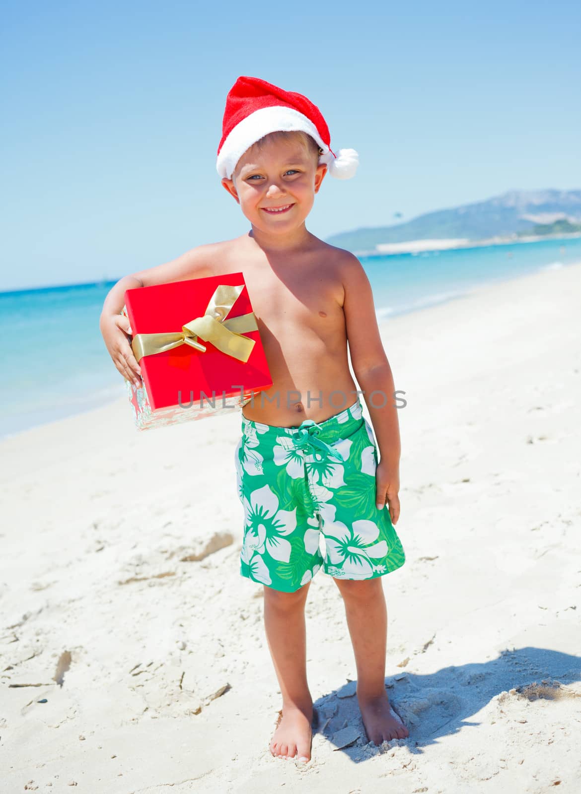 Cute little boy in Santa hat with gift on tropical vacation