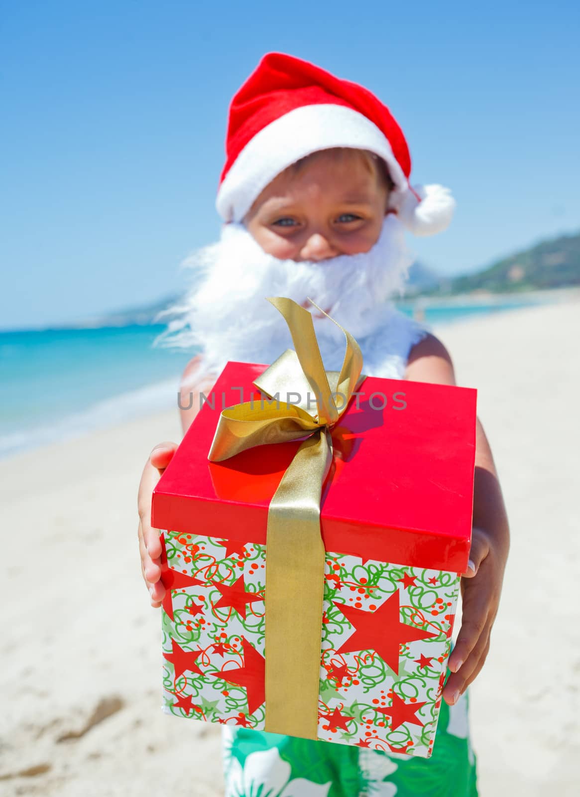 Cute little boy in Santa hat with gift on tropical vacation