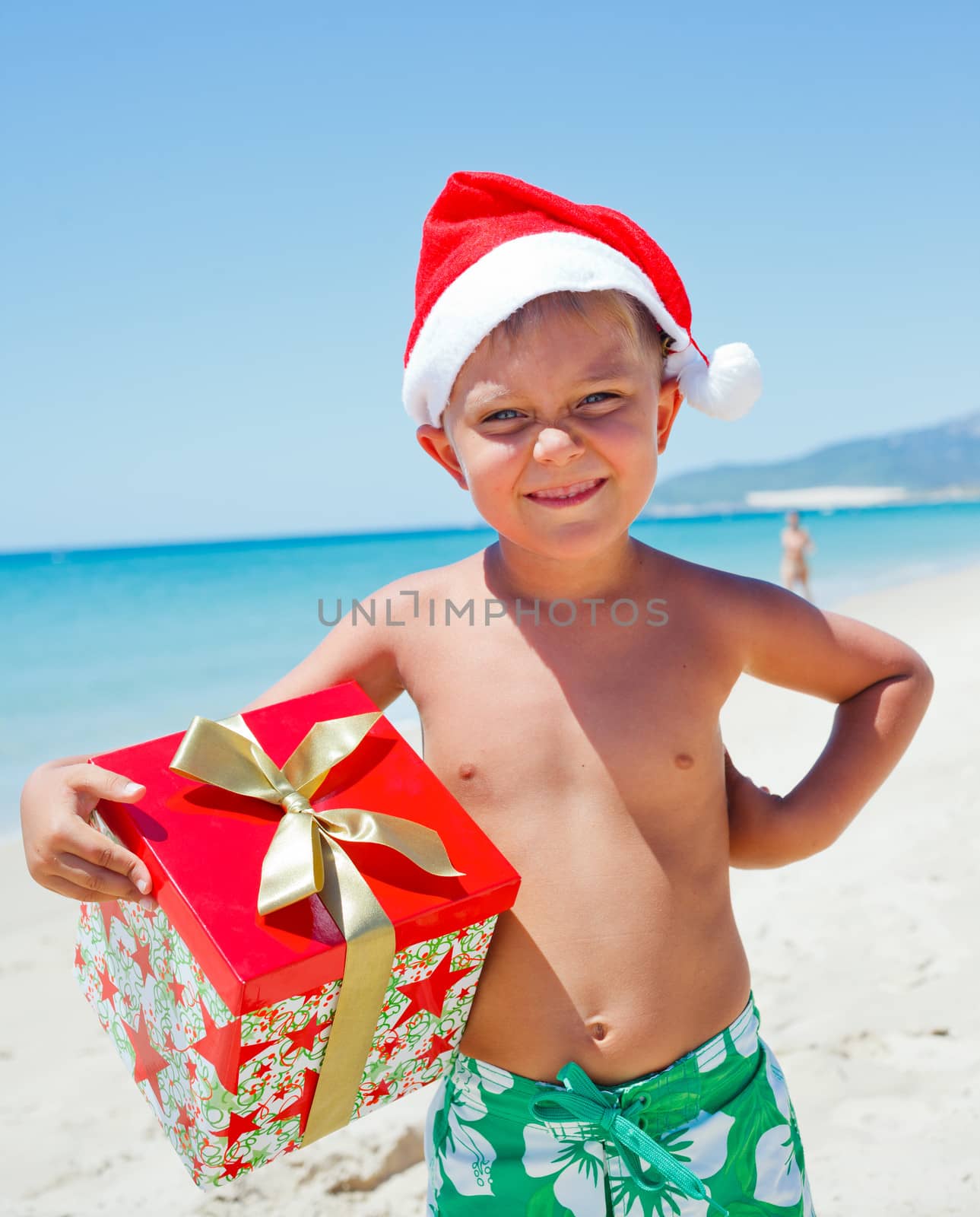 Cute little boy in Santa hat with gift on tropical vacation