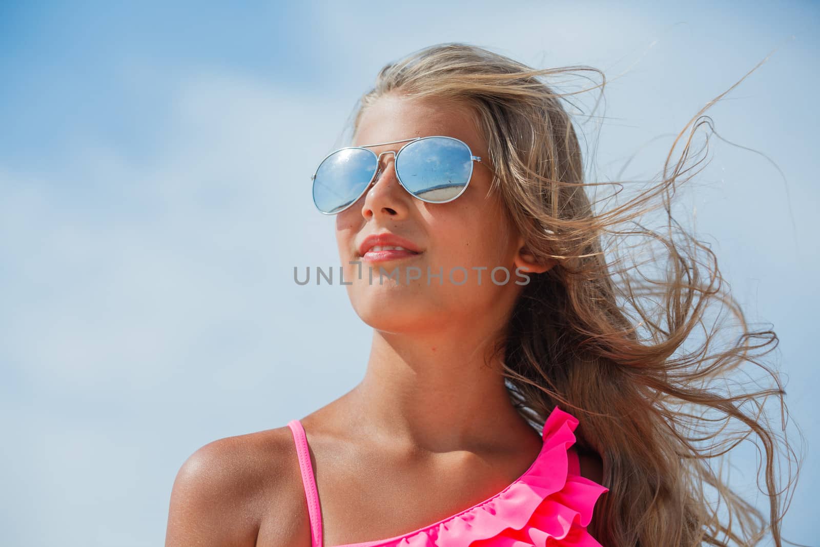 Beautiful blond girl in sunglasses on background blue sky