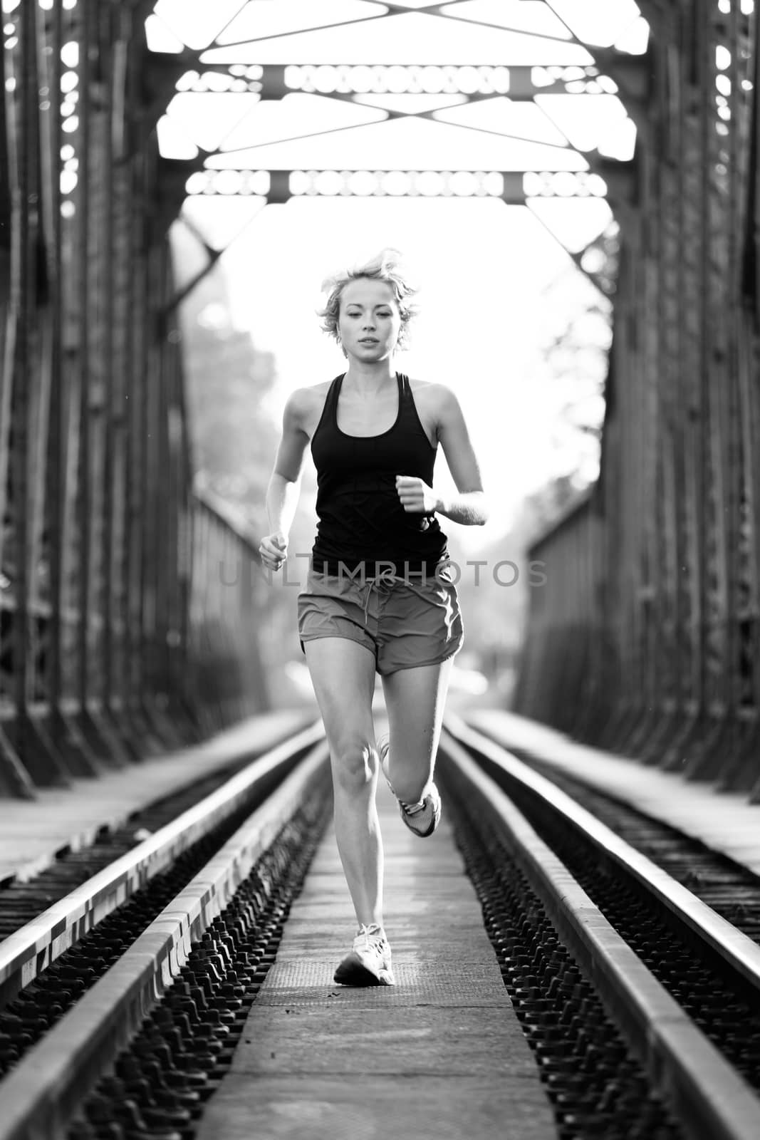 Athlete running on railaway tracks bridge in morning sunrise training for marathon and fitness. Healthy sporty caucasian woman exercising in urban environment before going to work; Active urban lifestyle.