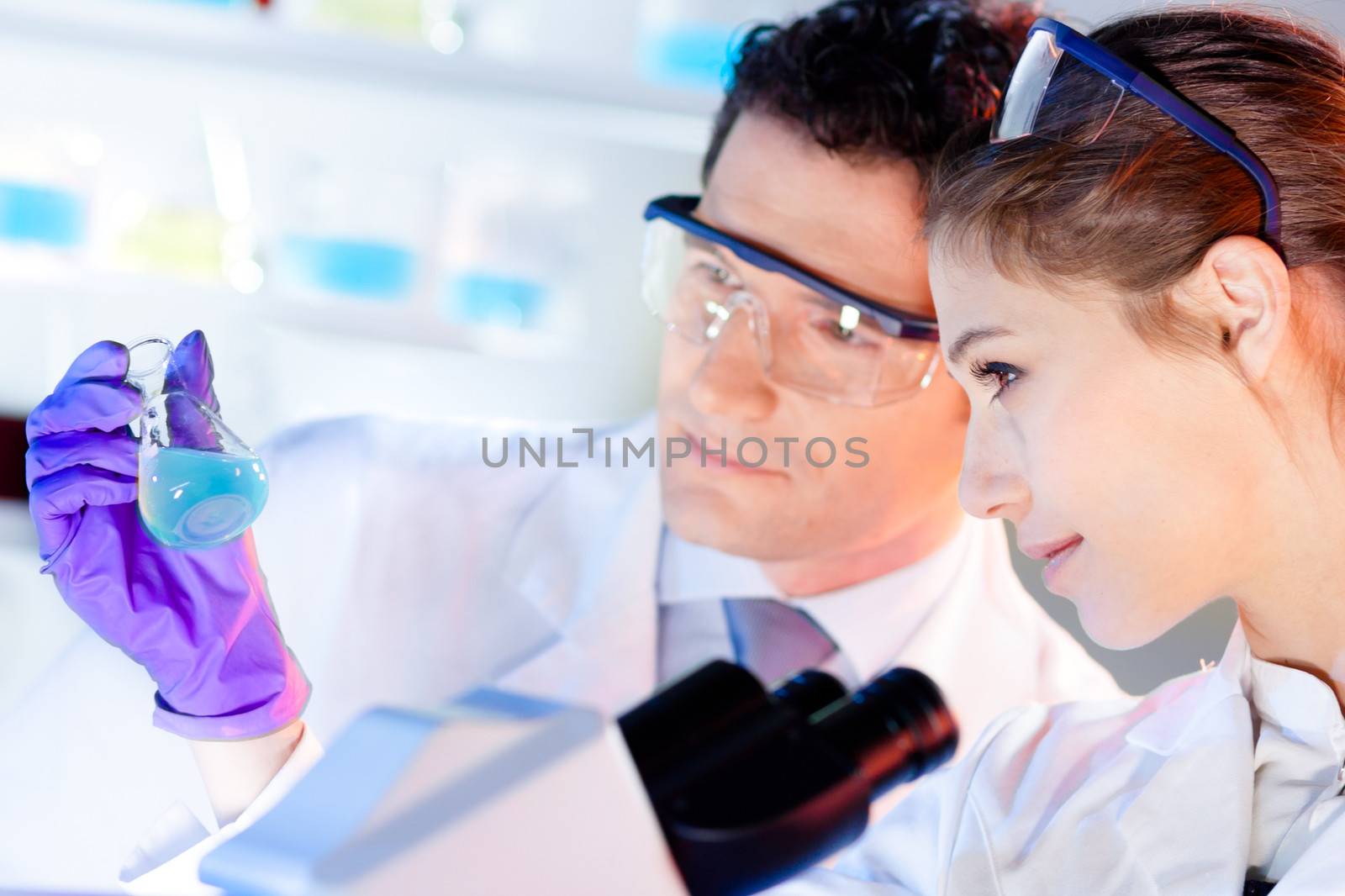 Chemical laboratory scene: attractive young student and her post doctoral supervisor scientist observing the green indikator solution color shift in glass flask.