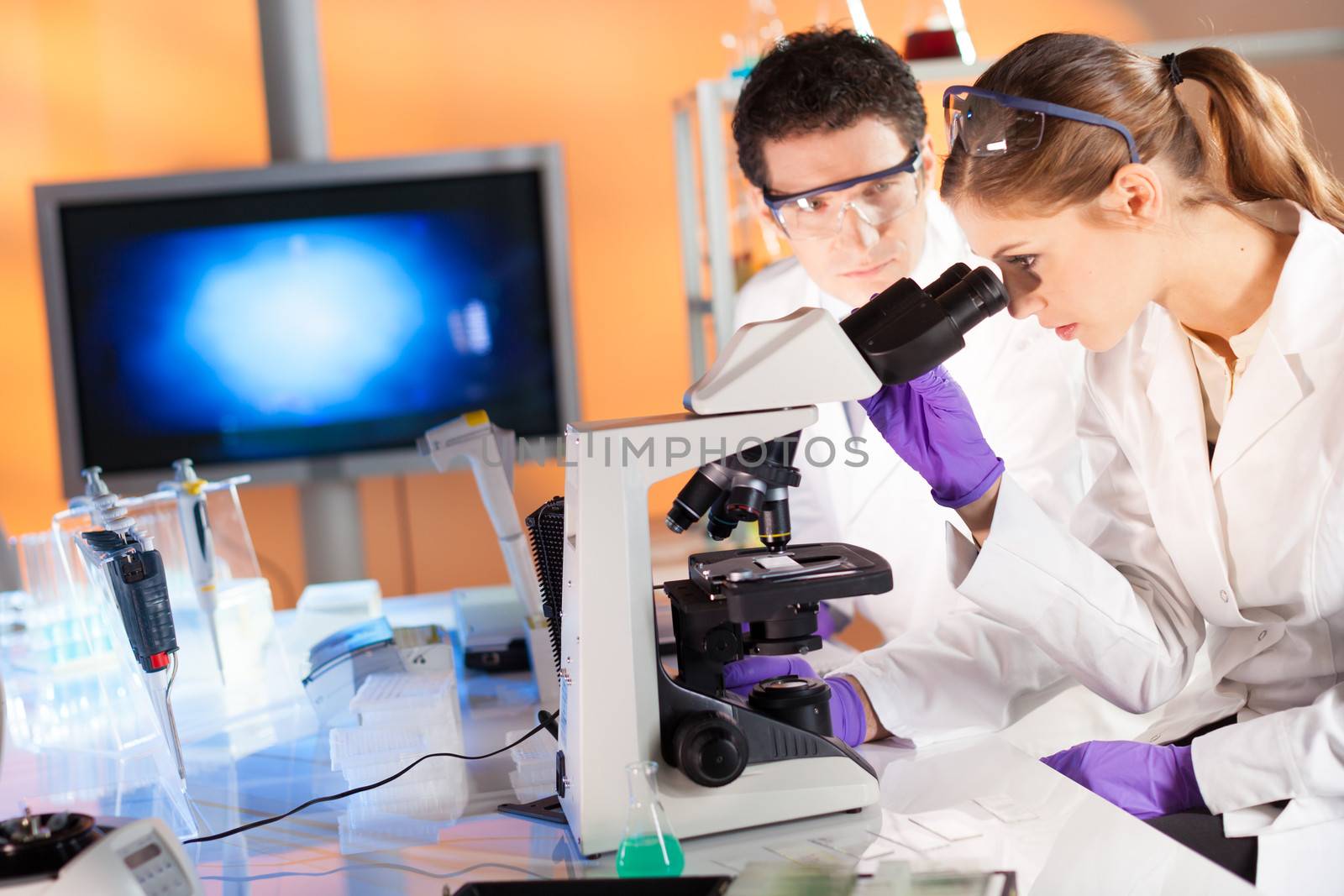 Attractive young scientist and her post doctoral supervisor looking at the microscope slide in the forensic laboratory.