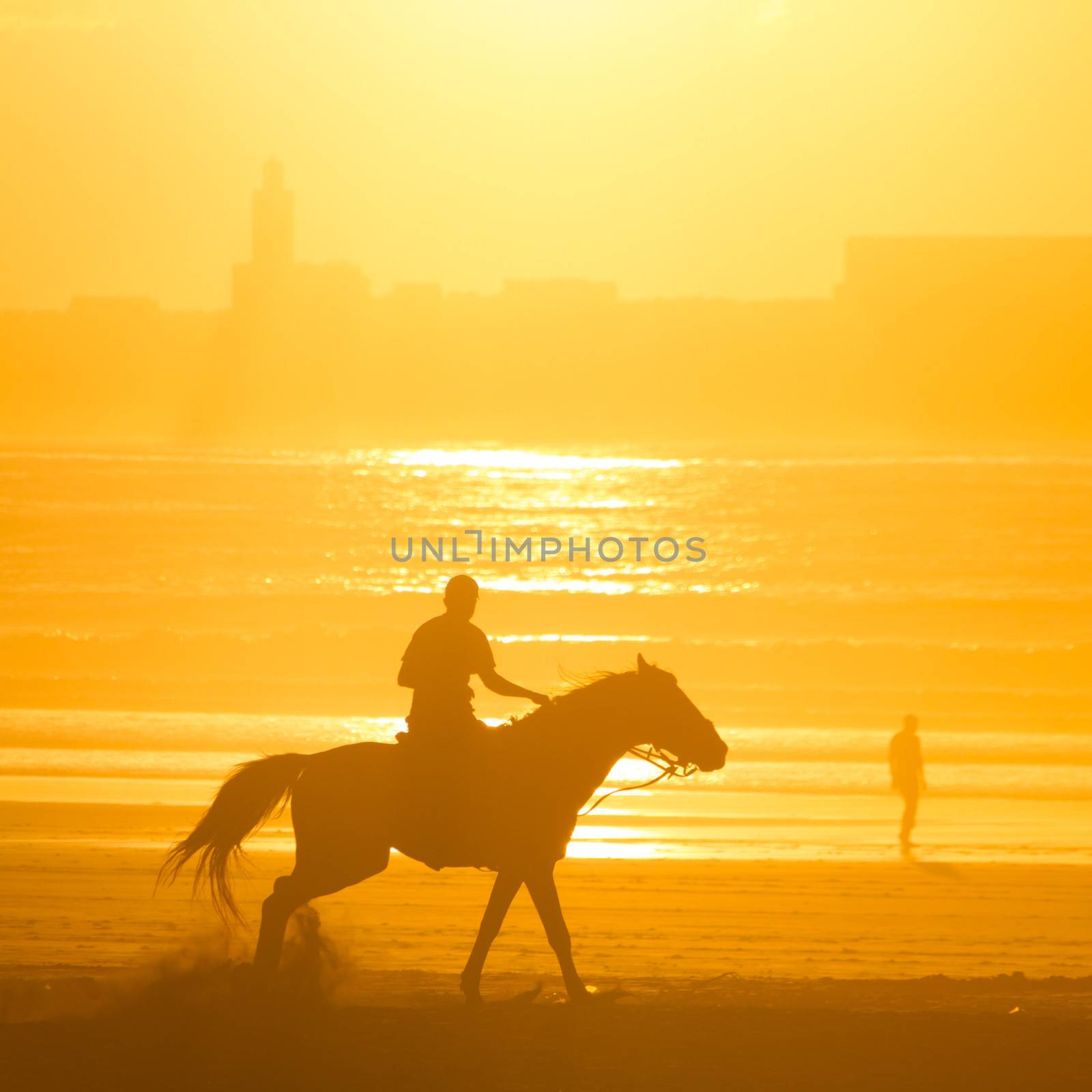 Man riding horse on the beach at sunset.