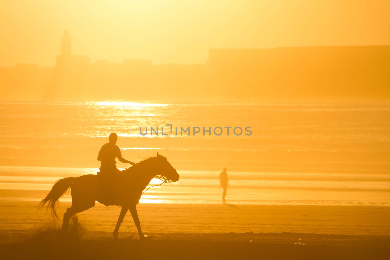 Man riding horse on the beach at sunset.