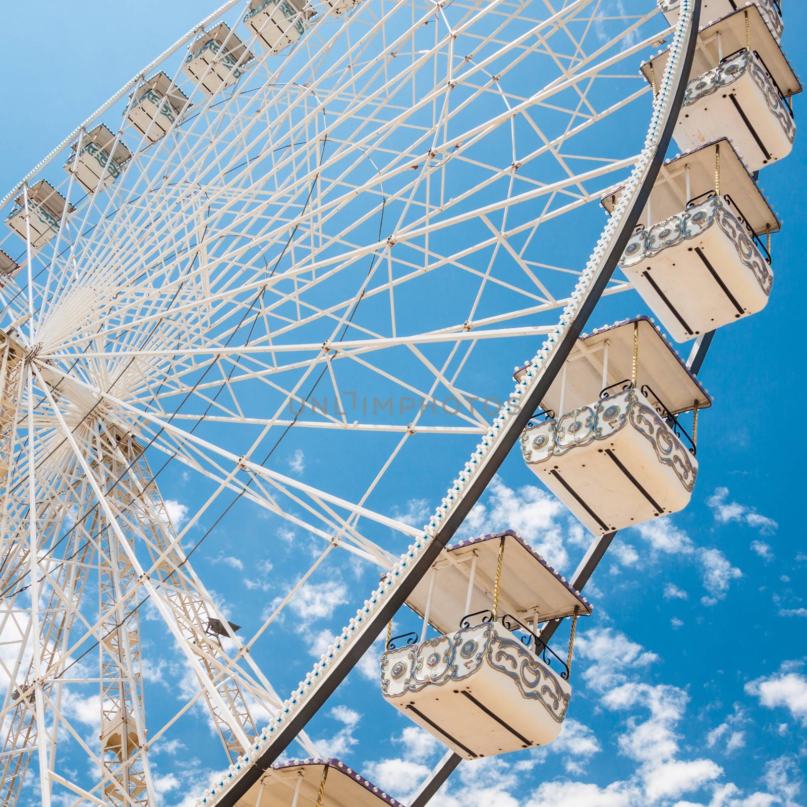 Ferris wheel of fair and amusement park.  White clouds in the blue sky in background.