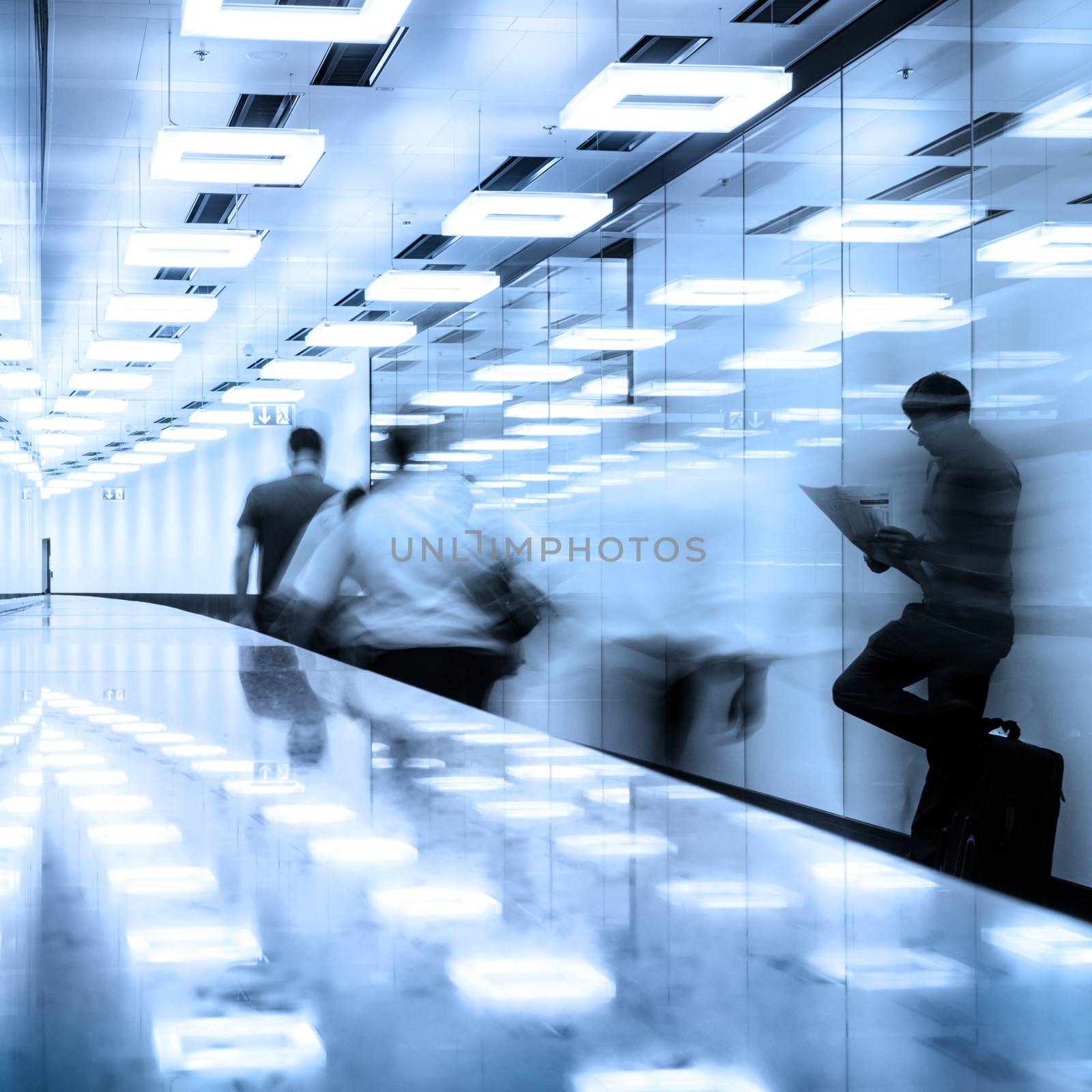 Business travelers  walking along contemporary illuminated airport terminal hall.