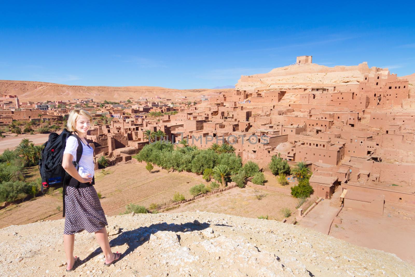 Adventurous woman in front of at Ait Benhaddou, fortified city, kasbah or ksar, along the former caravan route between Sahara and Marrakesh in present day Morocco.