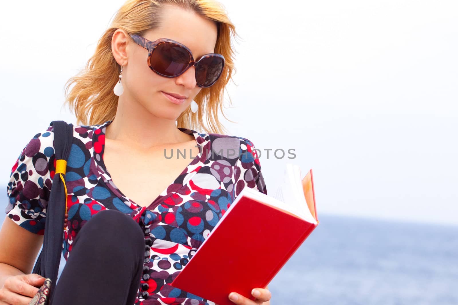 Attractive young lady reading a book by the sea.