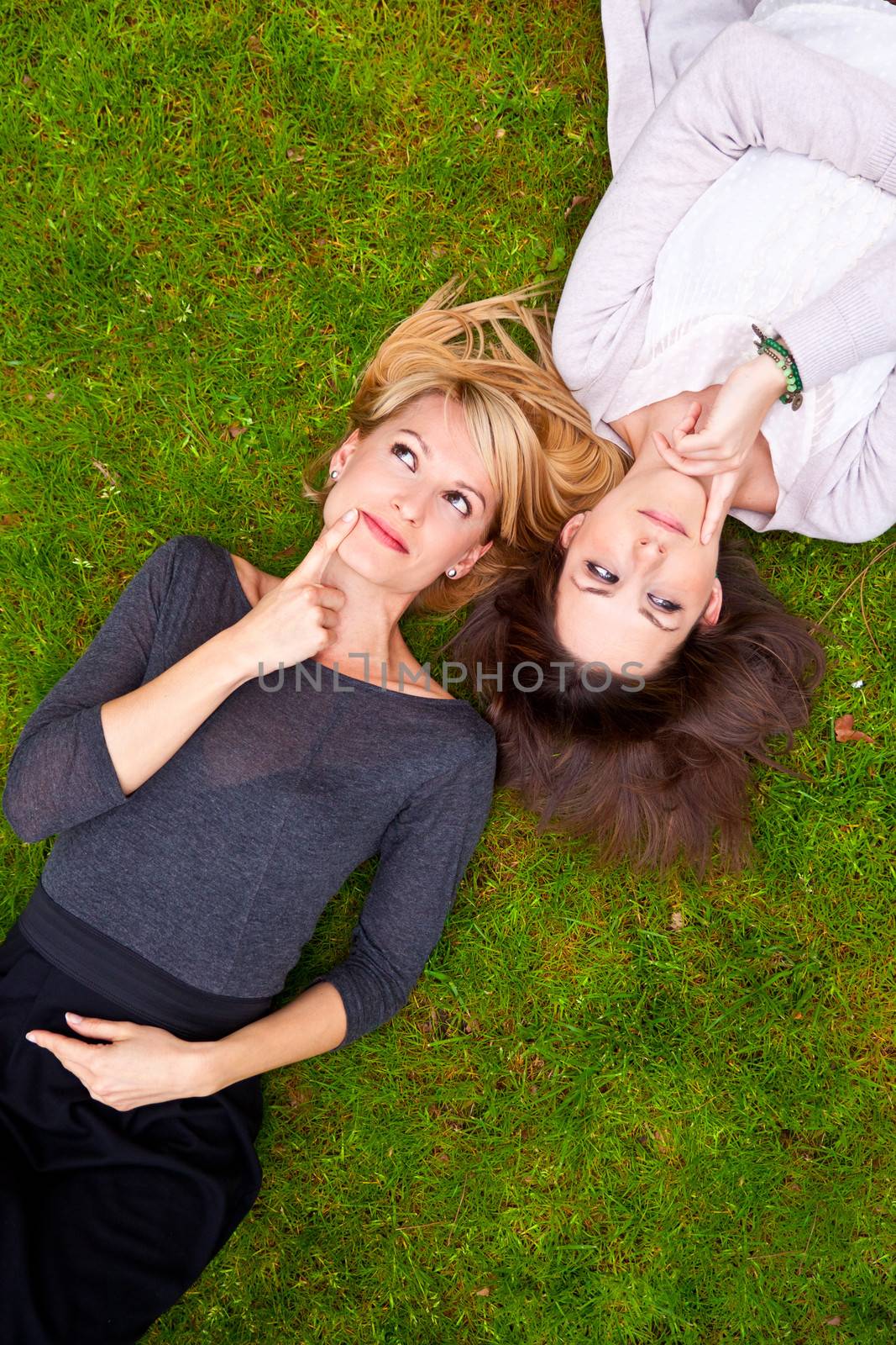 Two thoughtful girls lying in the grass have an smart idea.