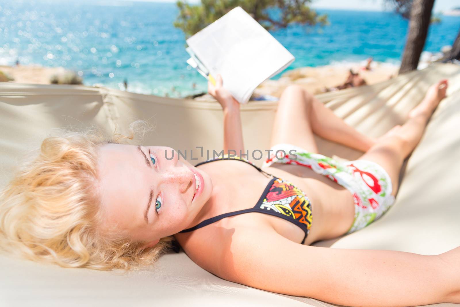 Beautiful girl lies on hammock on the beach and reads the magazine.