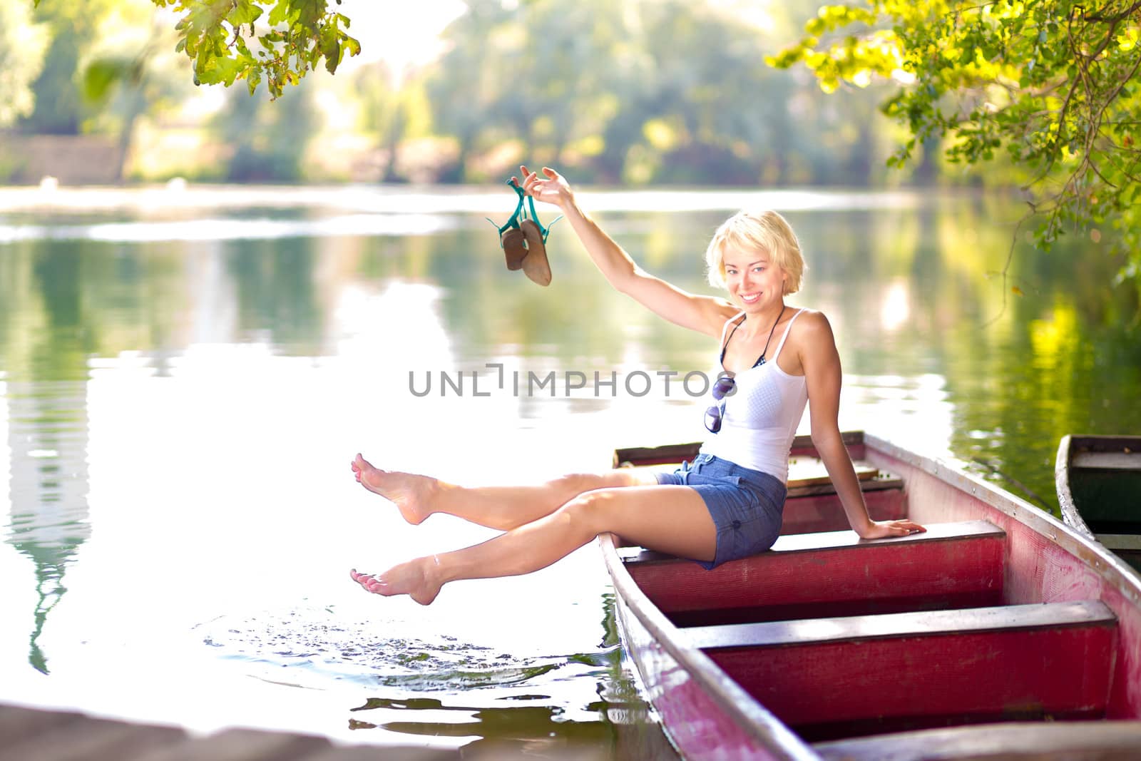 Carefree young blonde woman enjoying the sunny summer day on a vintage wooden boats on a lake in pure natural environment on the countryside.