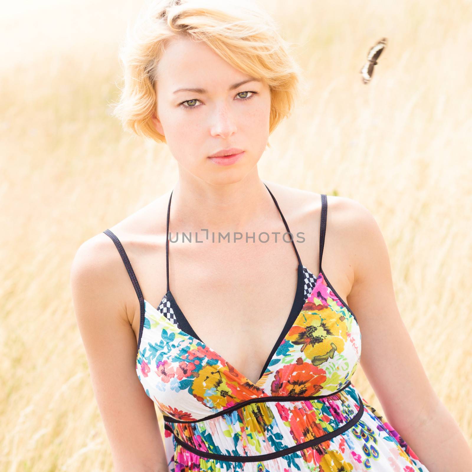 A portrait of a casual dressed beautiful young Caucasian woman outdoor in the meadow on a sunny summer day.