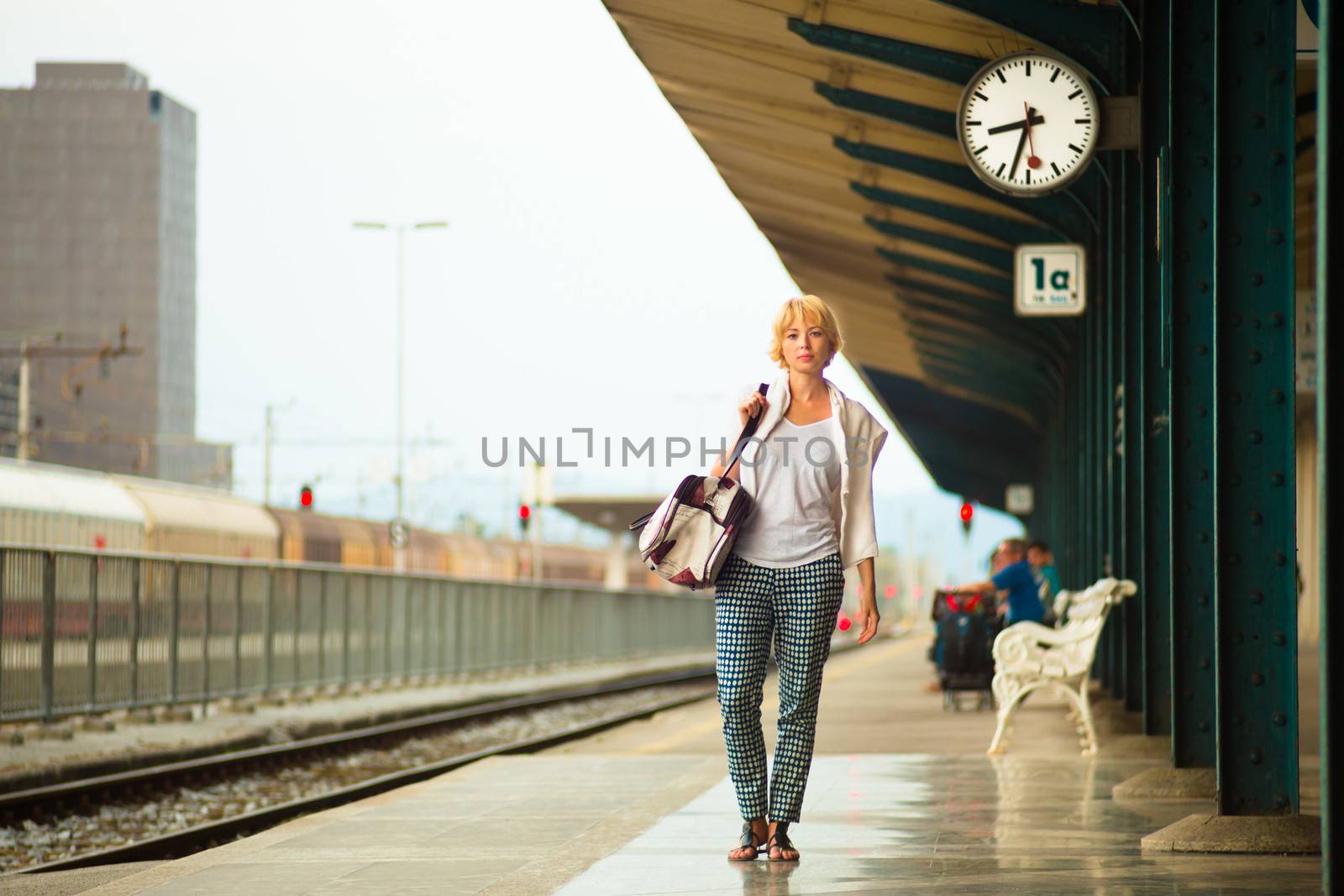 Blonde caucasian woman waiting at the railway station carrying bag.