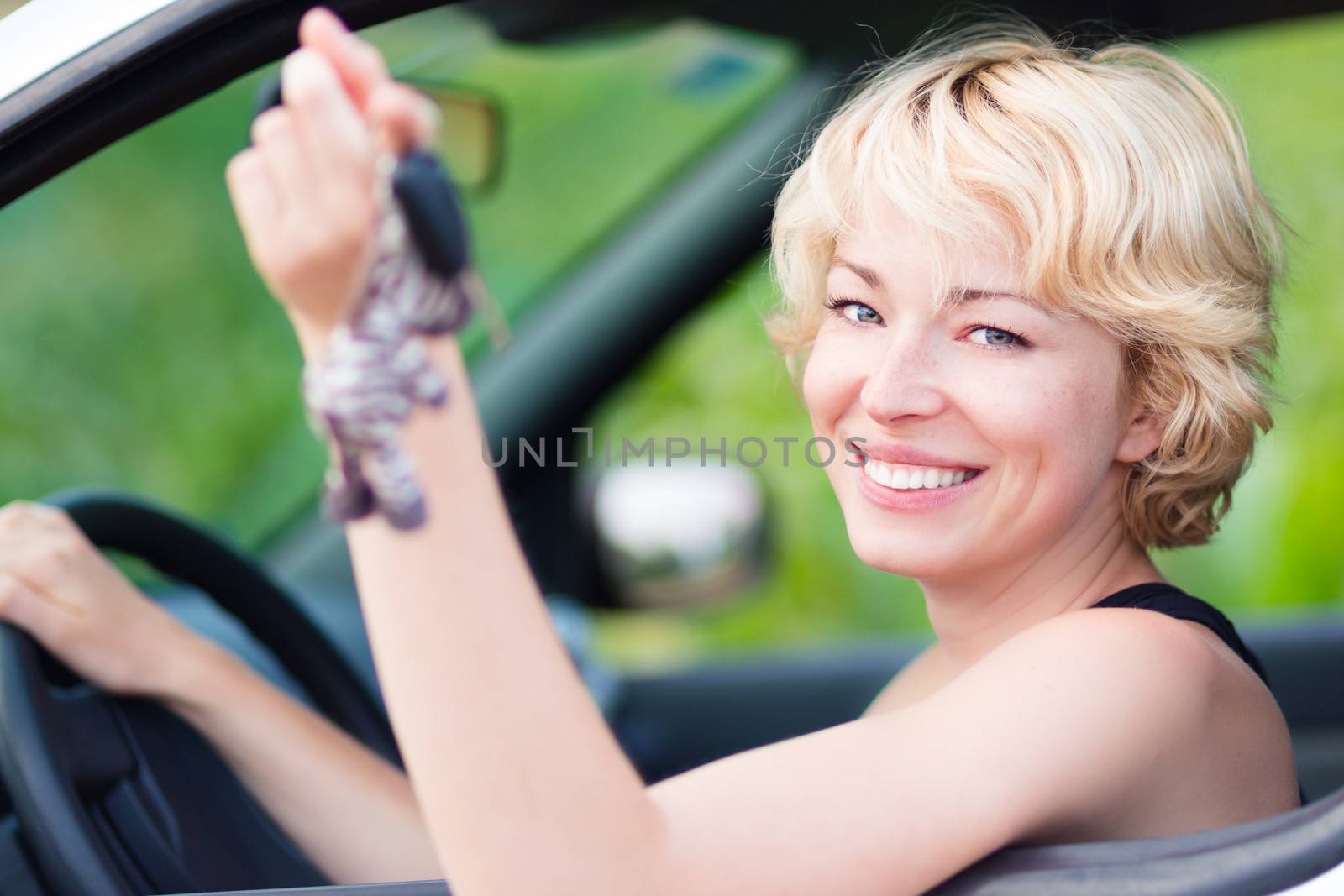 Woman, driving showing car keys out the window. Young female driving happy about her new car or drivers license. Caucasian model.