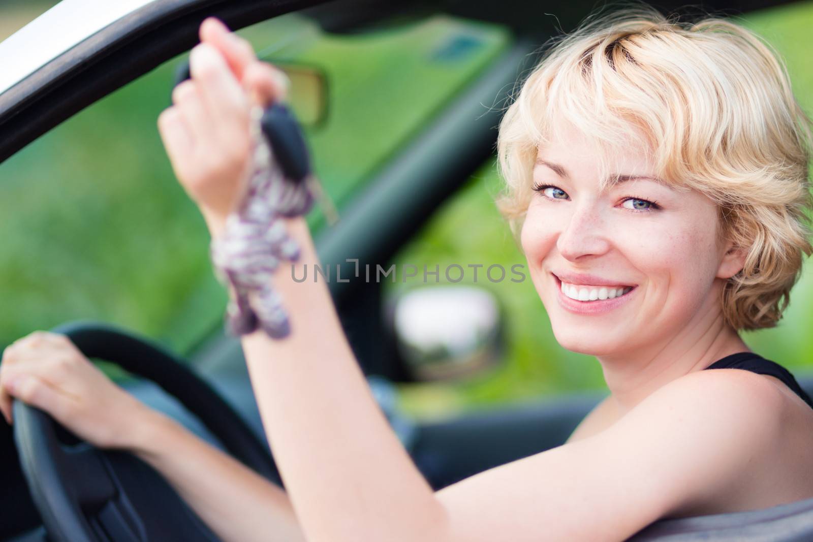 Woman, driving showing car keys out the window. Young female driving happy about her new car or drivers license. Caucasian model.