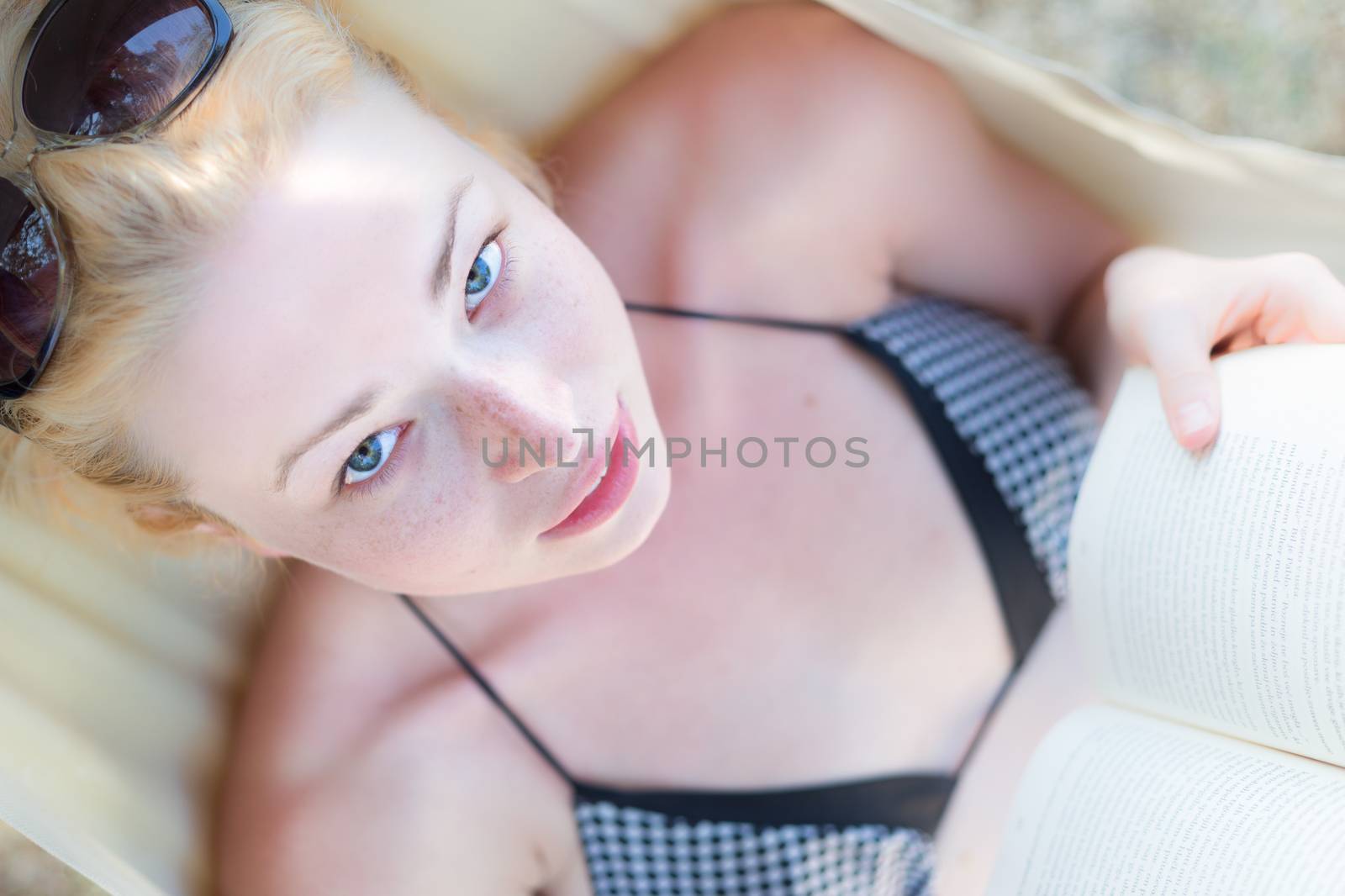 Beautiful girl lies on hammock on the beach and reads the book.