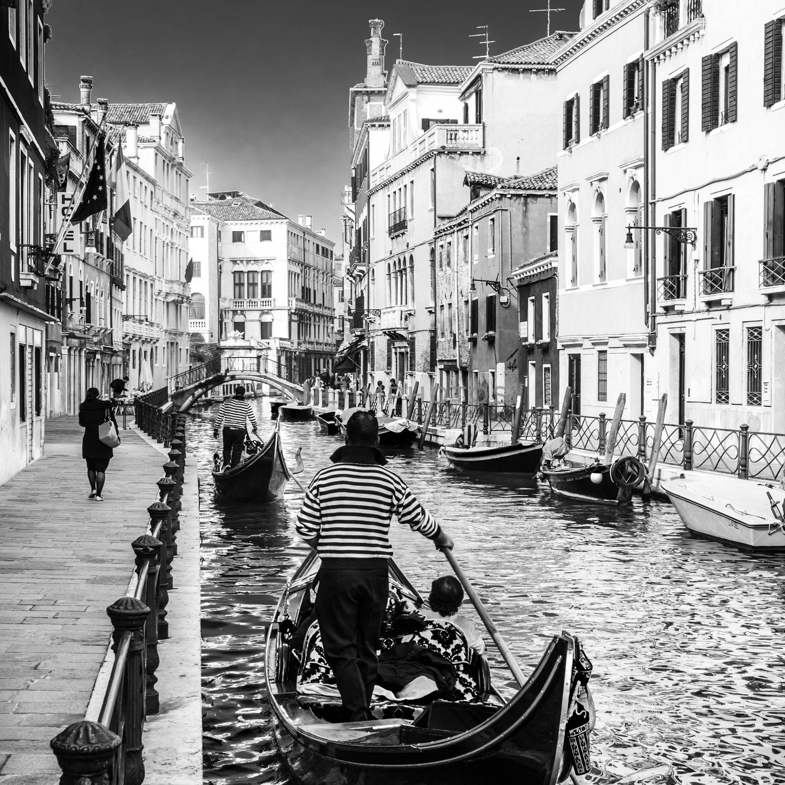 Gondolas passing on small canal among old historic houses and bridge in Venice, Italy. Black and white image.