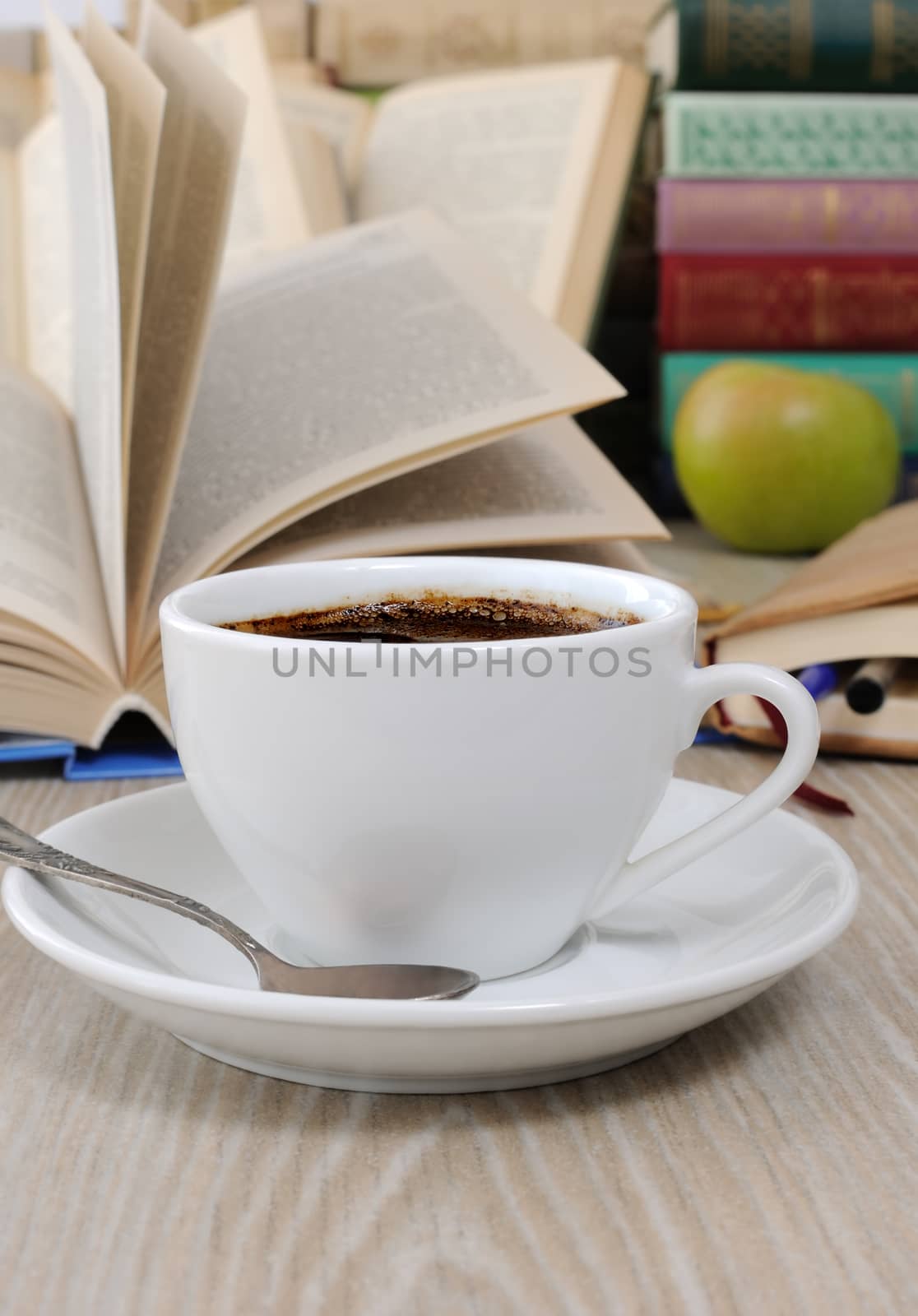 A cup of coffee on a table among books by Apolonia